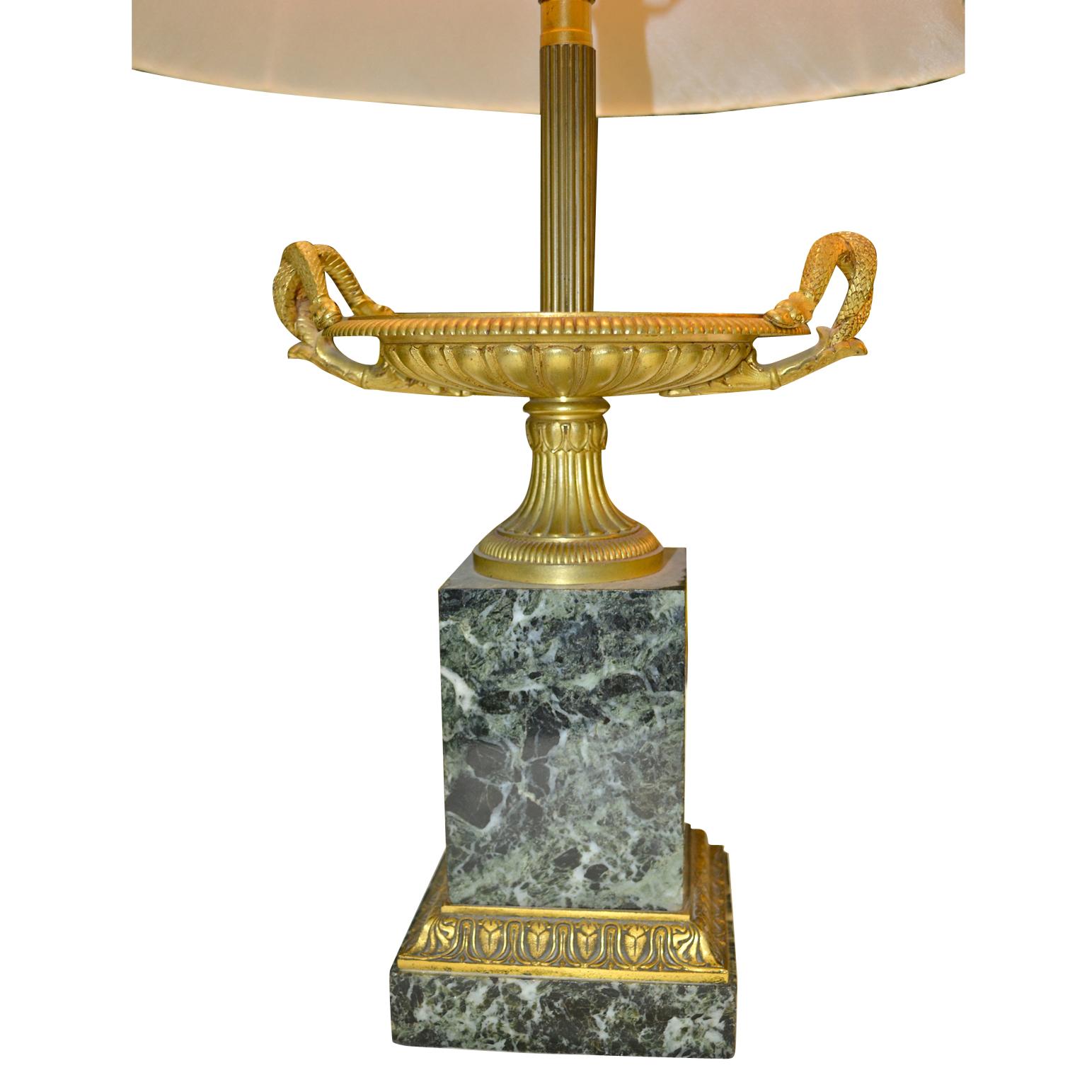 A pair of classical twin handled mid-19th century tazzas converted into lamps; the sea green marble bases with gilt bronze trim support a gilded urn with twin handles in the form of snakes. Lamps come with green pleated silk shades.