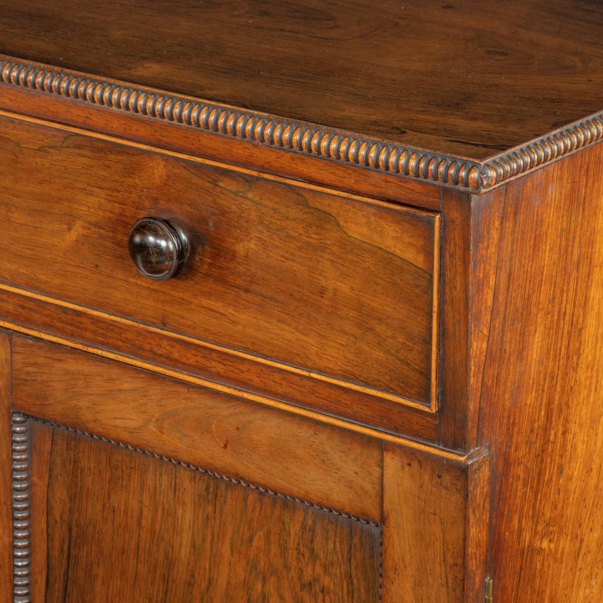 A pair of late Regency rosewood side cabinets, attributed to Gillows, each of rectangular form with two panelled doors below a single long frieze drawer, decorated with reel and bobbin beading, knob handles and turned, gadrooned feet. English, circa