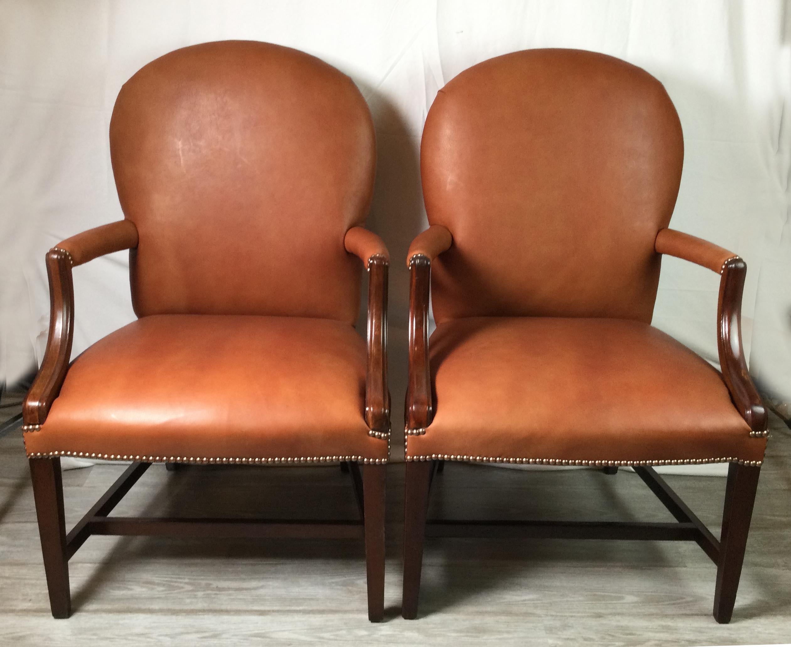 A pair of mahogany and leather open armchairs with new leather upholstery. The rounded backs with leather covered arms with attached leather seats.