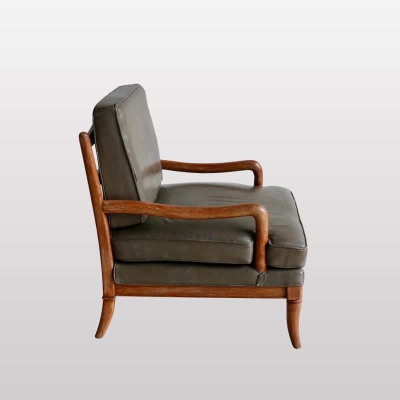 FRENCH work, 1950's
A pair of armchairs 
Ceruse oak frame on four round saber feet supporting an upholstered seat and a slatted back. Dark green leather-covered cushions.