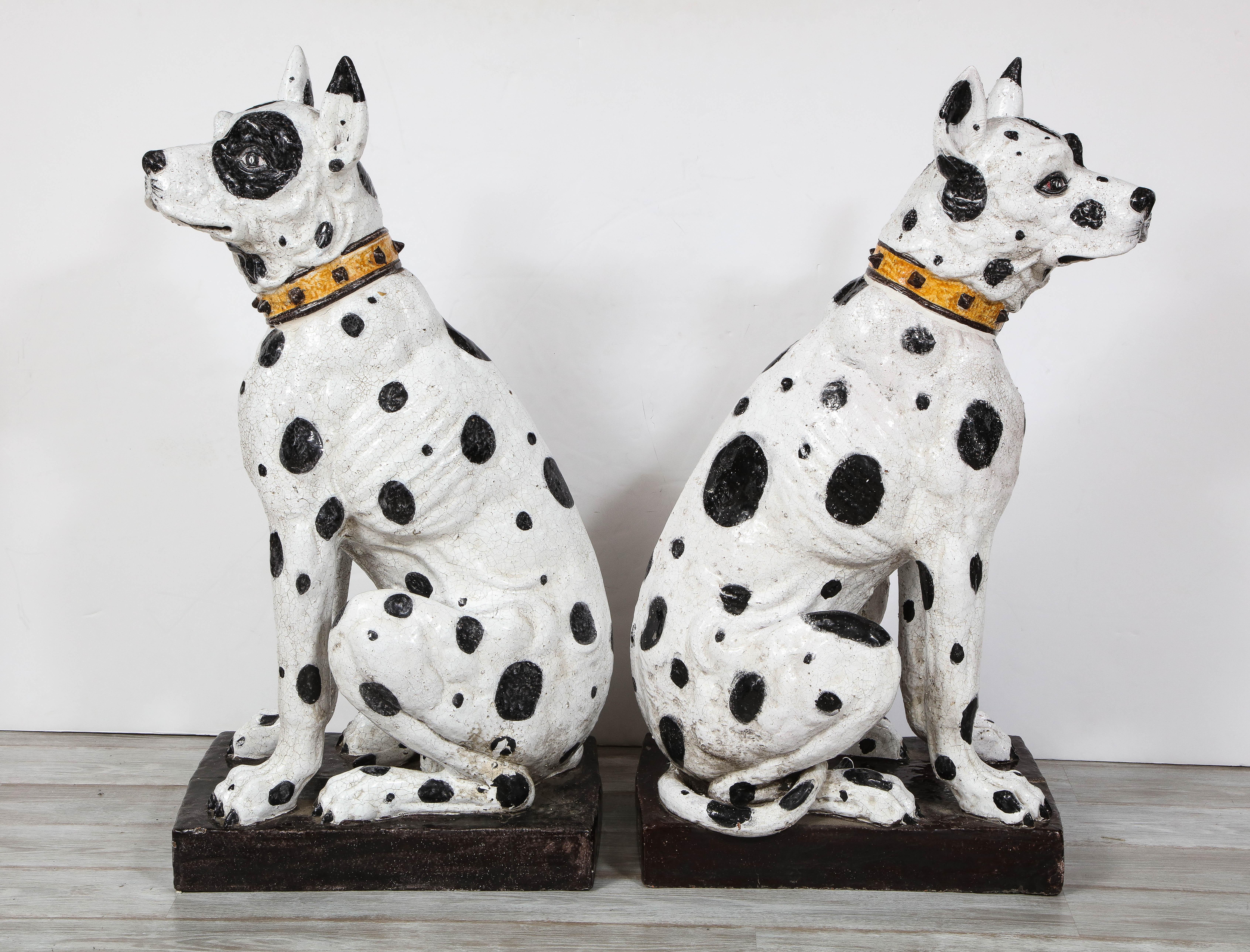 A majestic pair of Mid-Century Modern Italian life-size black and white ceramic Great Dane dogs depicted in two different seated stances on black bases that are exquisitely rendered in realistic anatomical details with sweet facial expressions.