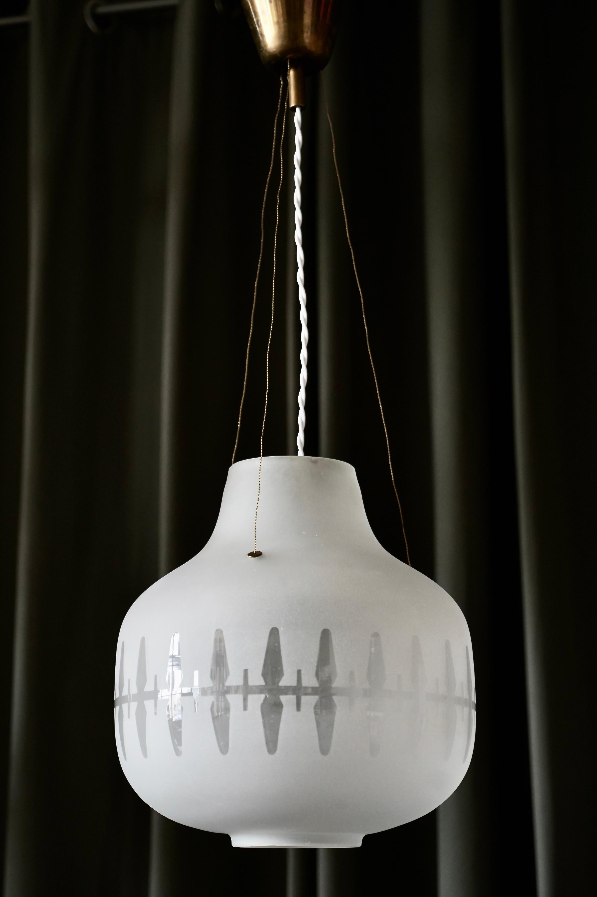 A pair of lighting pendants designed by Harald Notini for Arvid Böhlmarks Lampfabrik, Model 11868. Stockholm, 1950s. Double-etched shades with clear decoration, suspension in brass. Shade height 12.6