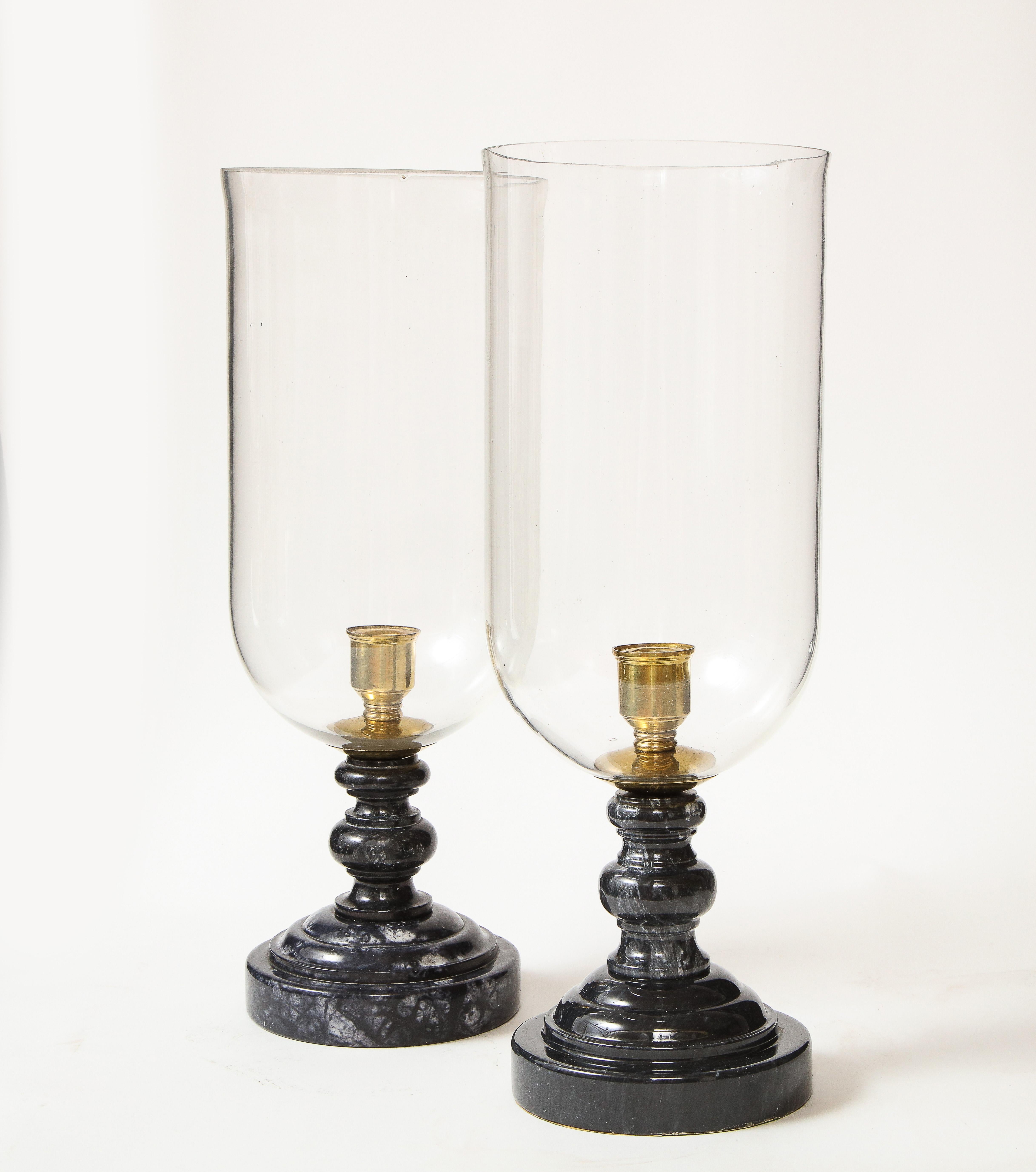 Each with a glass hurricane shade and rounded turned base of black marble with white veining.