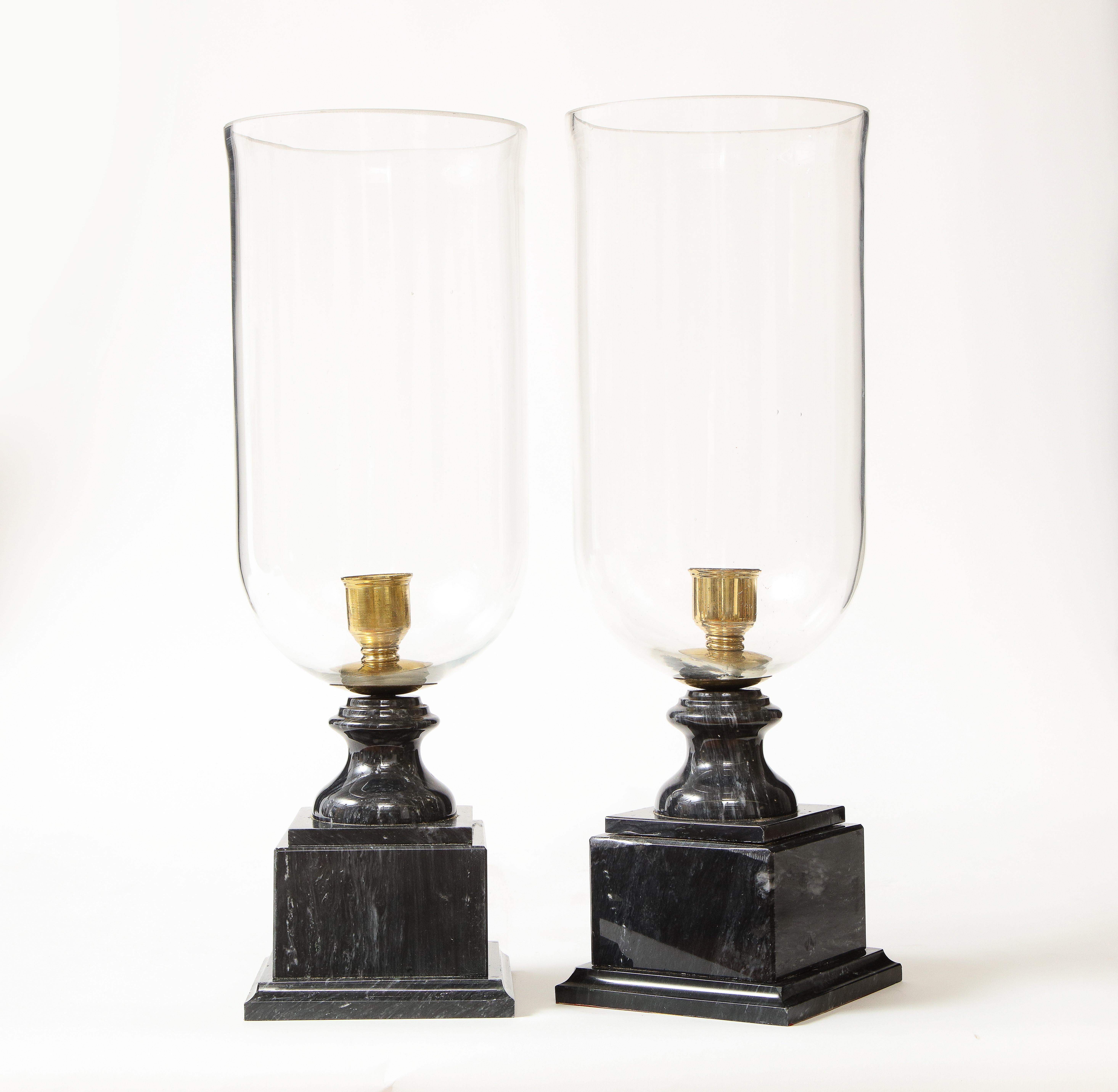 Each with a glass hurricane shade mounted on a turned polished black and white marble plinth base.