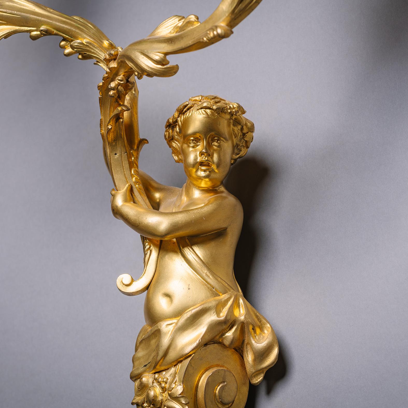 A Pair of Louis XIV Style Gilt-Bronze Twin-Light Wall-Appliques Modelled With Cherubic Herms. In the Manner of André-Charles Boulle.

Each modelled as a cherubic herm holding aloft acanthus branches. Wired for electricity.

France, Circa 1860.