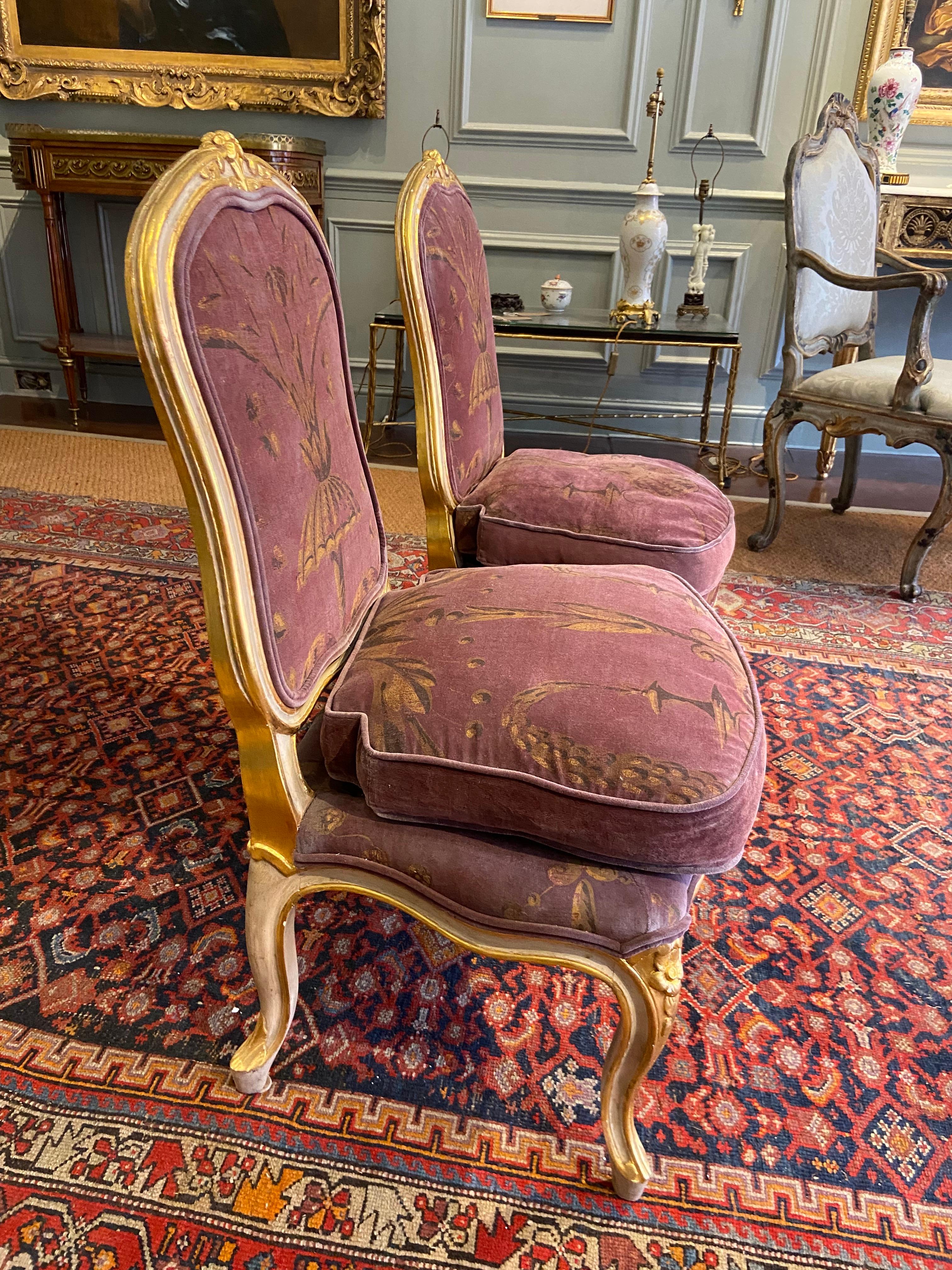 A Pair of Louis XV painted and gilded salon chairs (Mid 18th Century). Upholstered in plum-velvet and painted with floral motifs set on a gilded channelled frame with carved acanthus motifs.