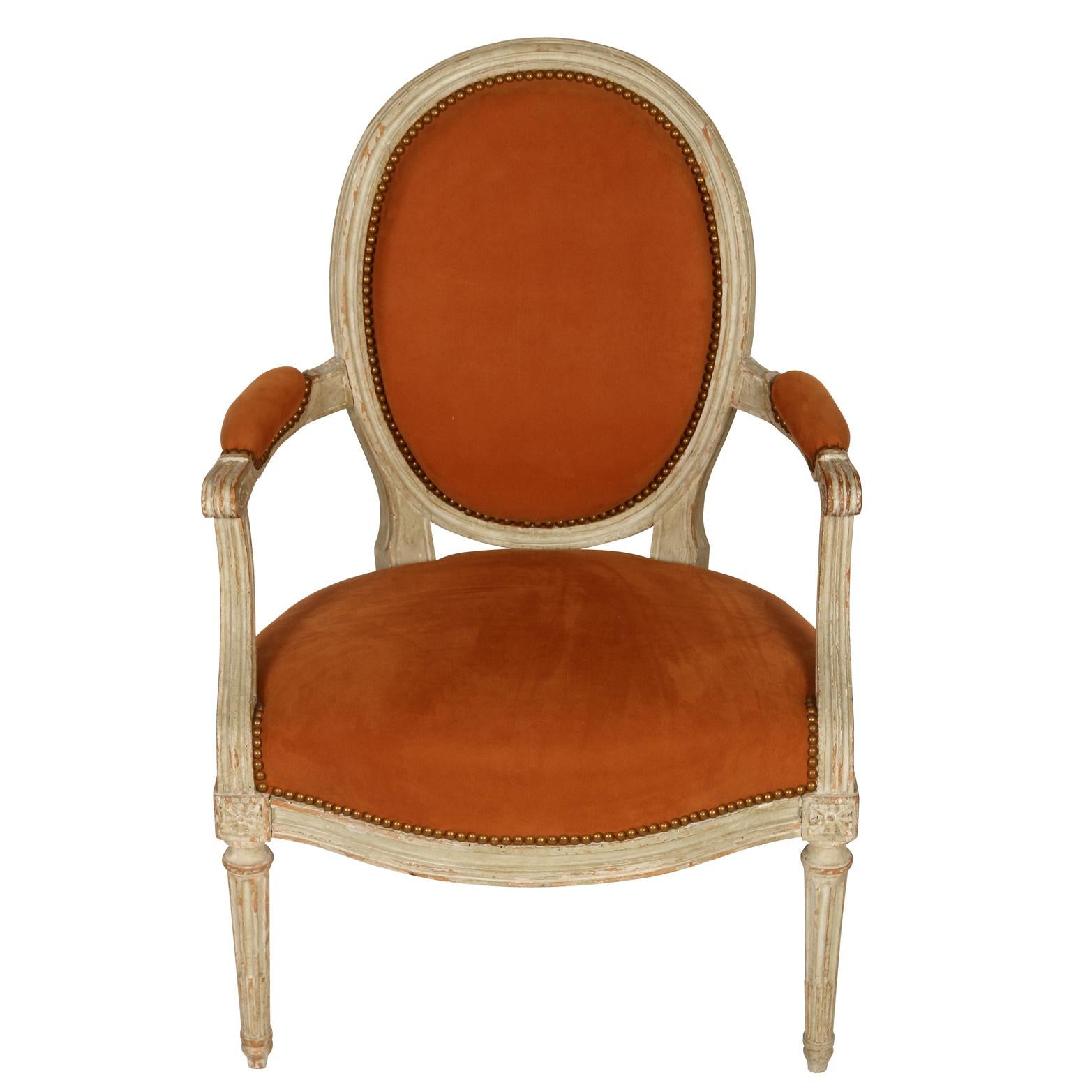 A pair of Louis XV painted fauteuils in cabriolet with straight reeded legs and oval backs, upholstered in orange suede with padded orange suede armrests.