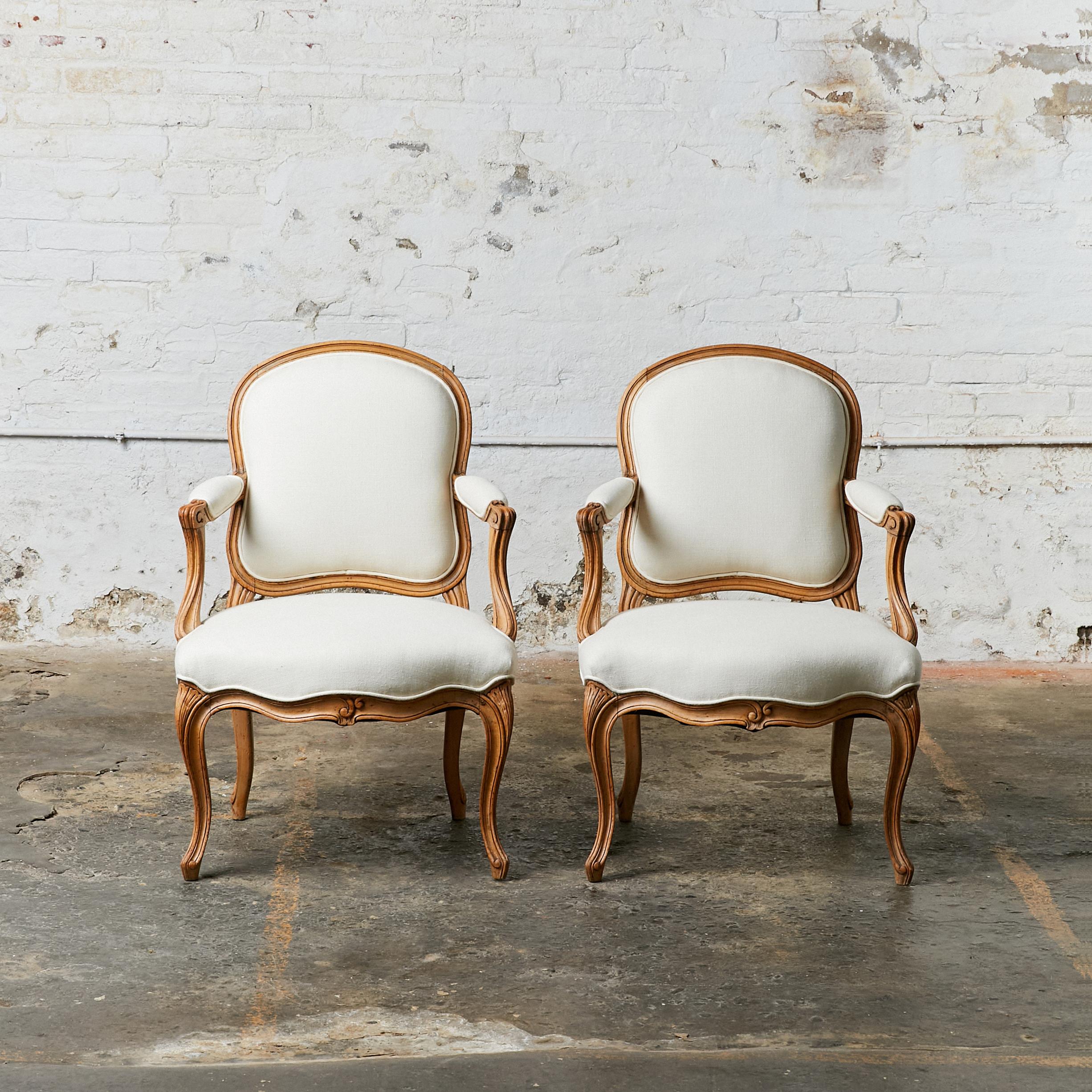 Set of two Louis XV style chairs with shaped back and open arm. The frame has been re-finished in the natural wood. Seat and back upholstered in off white linen with antique bronze studs.