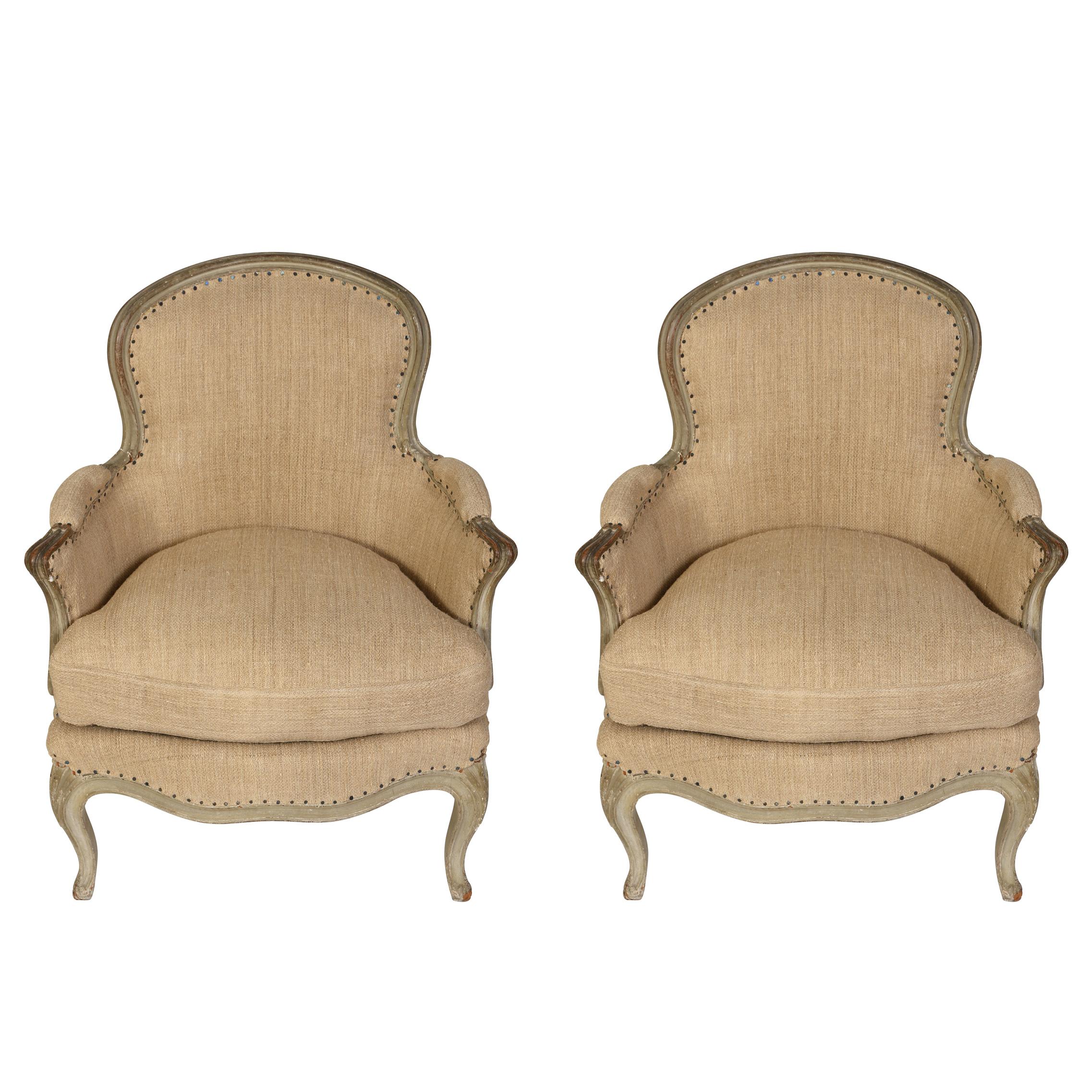 A pair of charming Louis XV style bergères with tight back, loose seat cushion, covered in a Belgian linen.  The frames are painted in a washed gray finish that has developed a soft patina.  The curved apron and cabriole legs are characteristic of