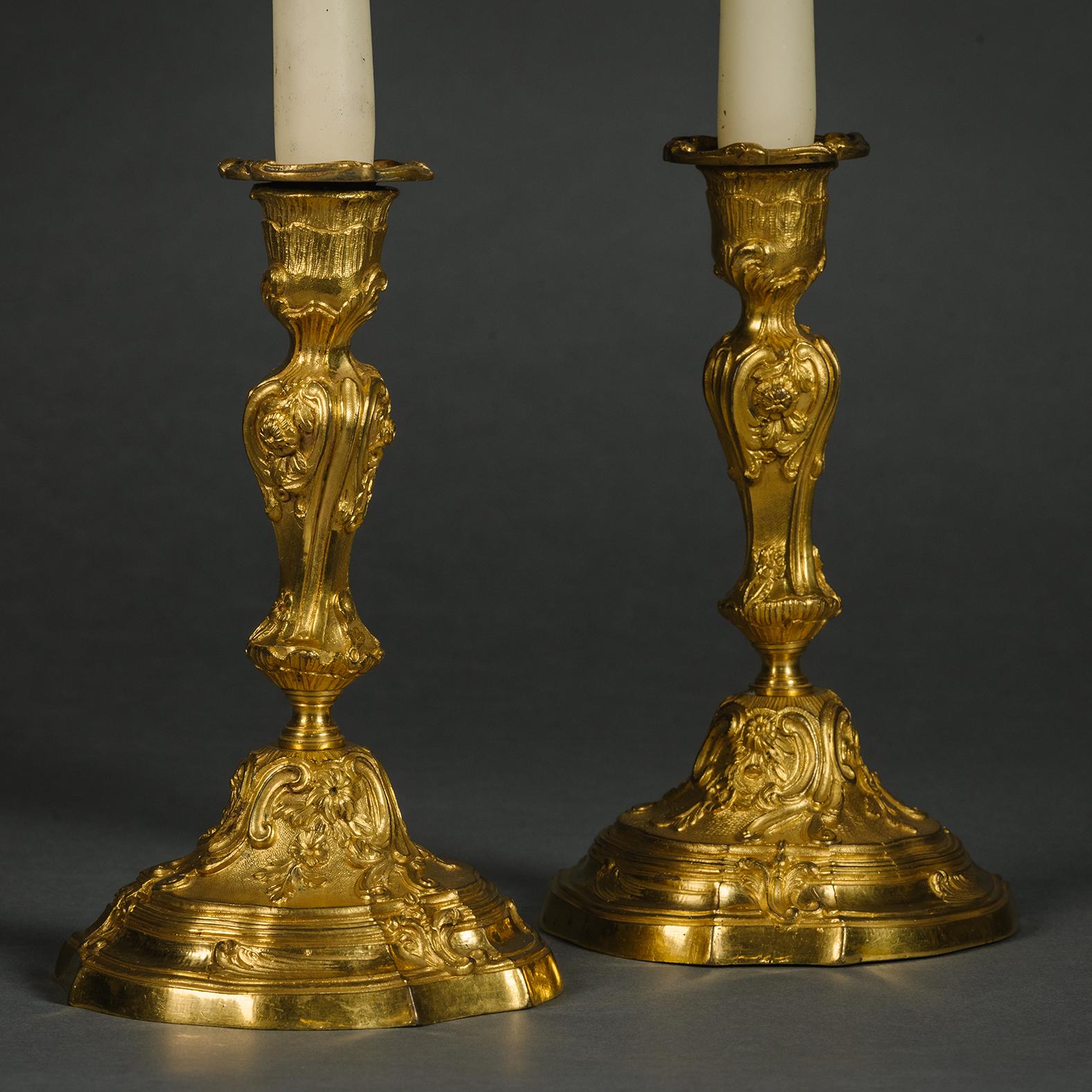 A Pair of Louis XV Style Candlesticks. 

Each baluster stem cast with C-scrolls and  below a nozzle and drip-pan, on a spreading rocaille-cast and moulded circular base

These charming candlesticks are designed in the manner of Juste-Aurèle