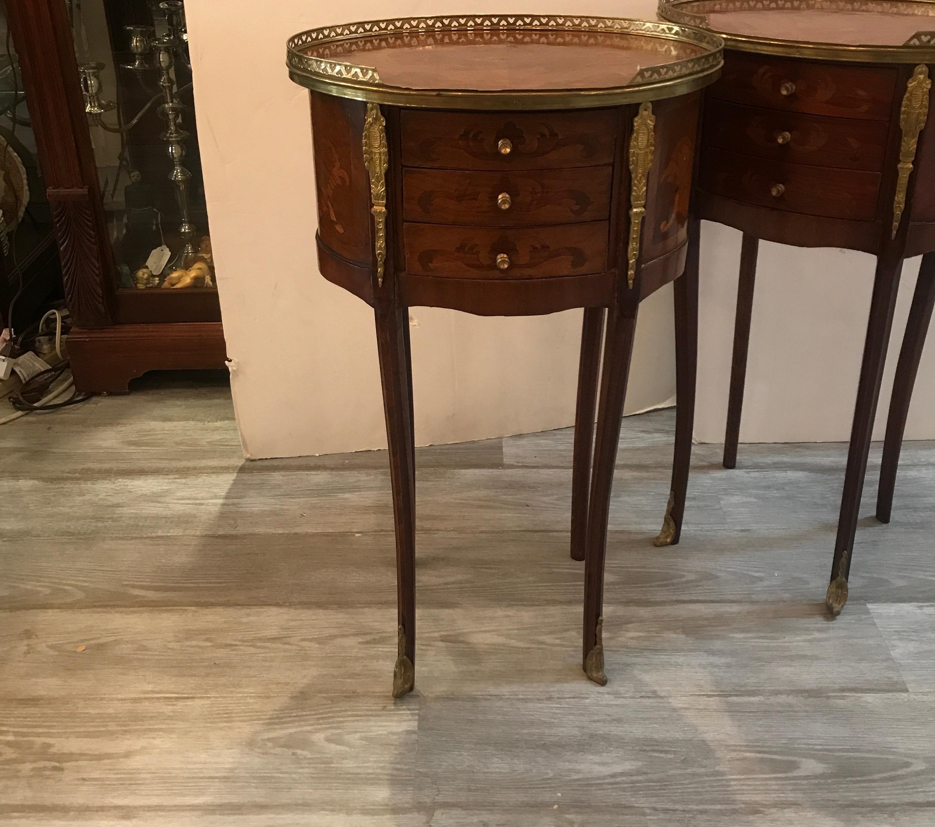 A pair of French Louis XV style oval table stand with three small drawers. The tops with oval inlay detail with reticulated brass gallery edge. Each with four gracefully shaped tapering legs, circa 1920s diminutive size 29 inches high, 17 inches