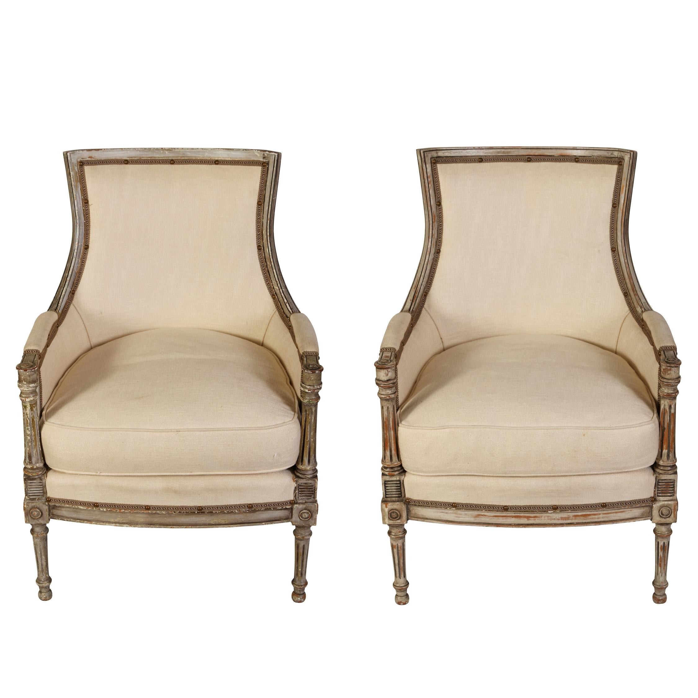 A pair of elegant Louis XVI style bergères with a squared back and a loose seat cushion.  The graceful chairs have many of the lovely details characteristic of the Louis XVI style, including subtle carving, fluted arm supports, tapered fluted legs,