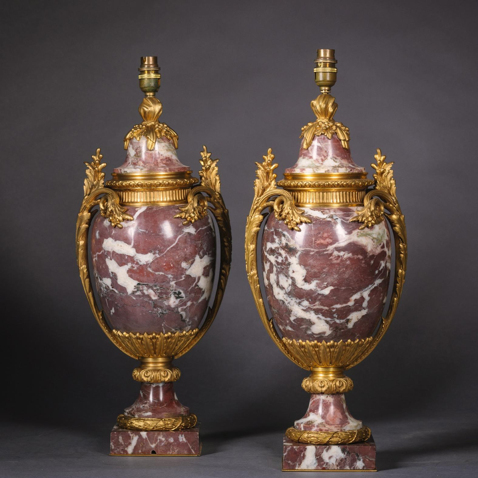A pair of Louis XVI style gilt-bronze mounted fleur de pêcher marble vases, now mounted as lamps. 

The body of each vase is of ovoid shape with a fluted gilt-bronze collar and domed top with berried finial and scrolling and fronded acanthus cast