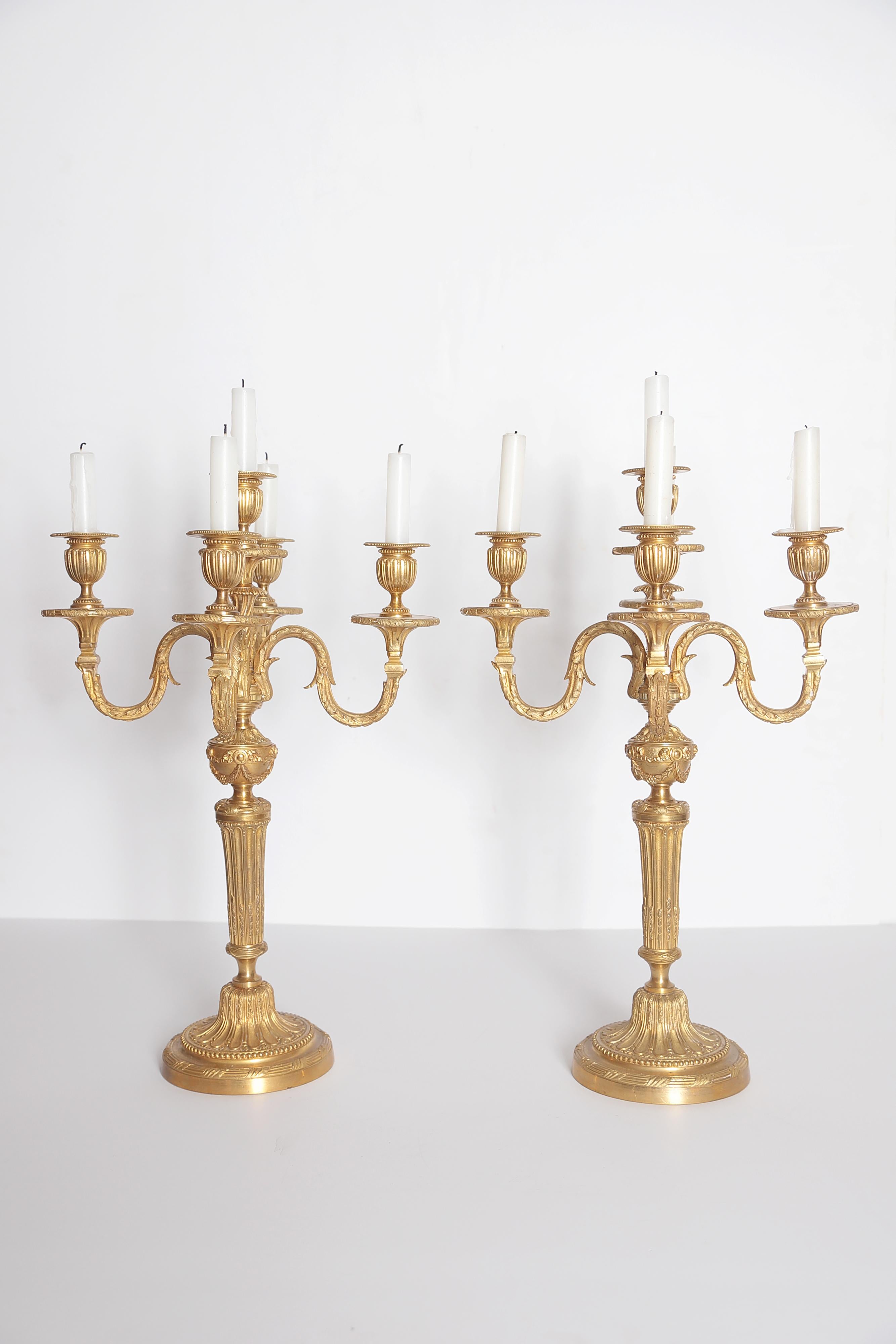 An elegant pair of Louis XVI style gilt bronze candelabra, columnar form on round base with center candleholder and four branches / arms, classical decoration overall

several individual parts / pieces are stamped 1065 and E G.

Measures: 6.5