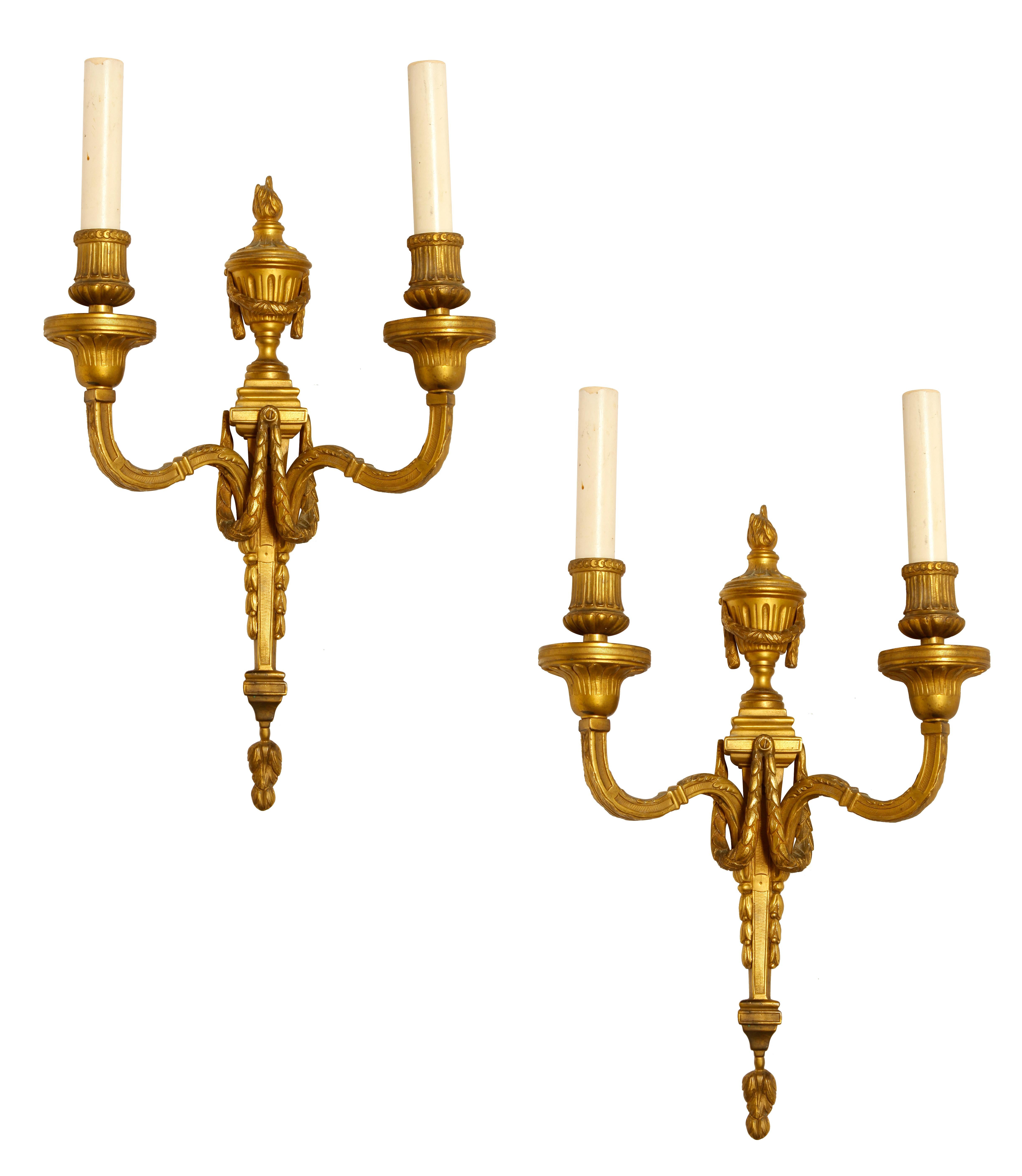 A pair of Louis XVI style gilt bronze sconces, each with two arms and a center torch and a regal garland joined in the center of the wo arms.  Recently rewired and polished.