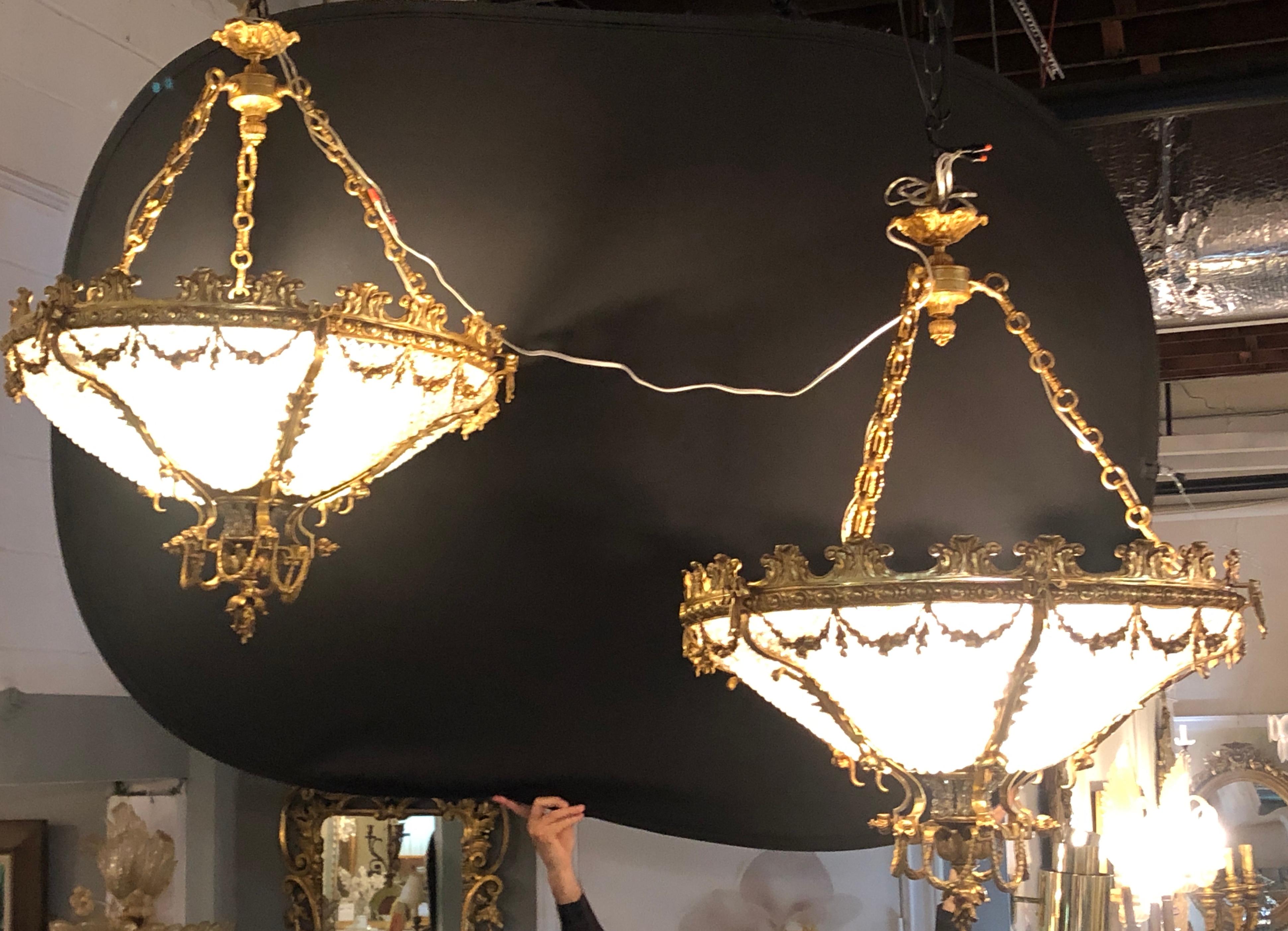 A pair of large and impressive doré or gilt bronze Louis XVI style beaded chandeliers with bow-tie decoration. These fine basket beaded chandeliers have a wide crystal basket framed in a doré bronze frame of scroll, floral and shell design. The