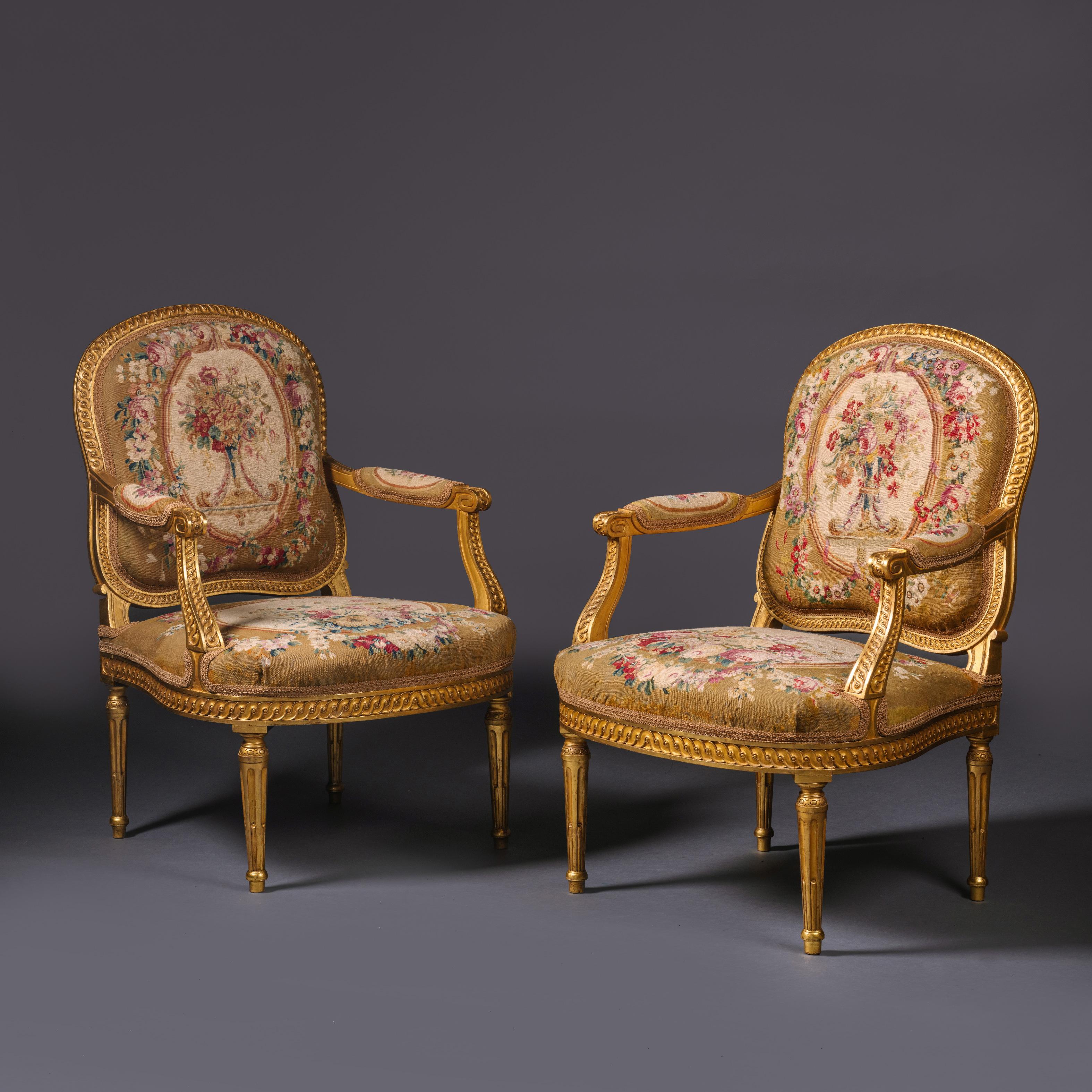 Ein Paar von Louis XVI Stil vergoldetem Holz und Wandteppich fauteuils.

Der Wandteppich stammt aus dem 18. Jahrhundert und wird der Manufaktur von Beauvais zugeschrieben. Die Rahmen sind fein geschnitzt und mit guillochierten Bändern versehen.