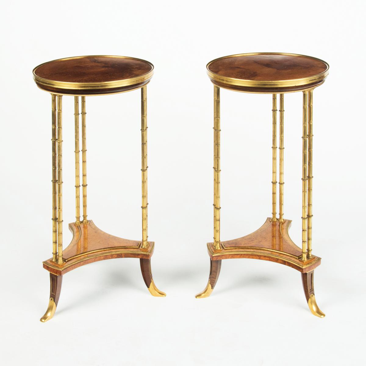 A pair of Louis XVI style mahogany and ormolu gueridons, after Adam Weisweiler, each with a circular amboyna veneered top and triform undertier enclosed within three pairs of simulated bamboo columns, with applied openwork bronze borders.  French,