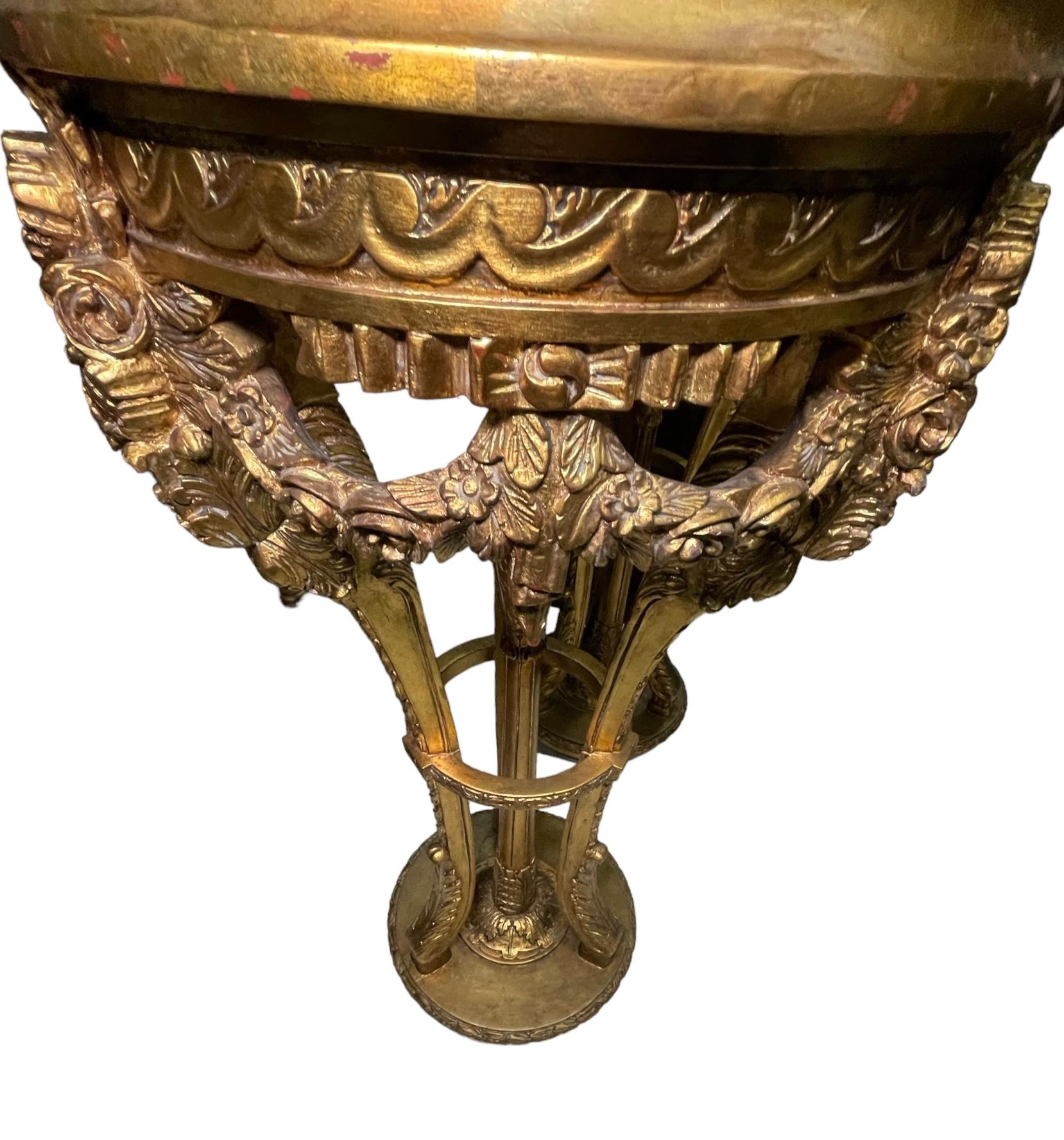Il s'agit d'une paire de piédestaux en marbre et bois doré de style Louis XVI. Il représente un plateau rond en marbre beige encadré de bois doré sur un trépied composé de pieds en cabriole décorés de feuilles d'acanthe sculptées à la main dans la