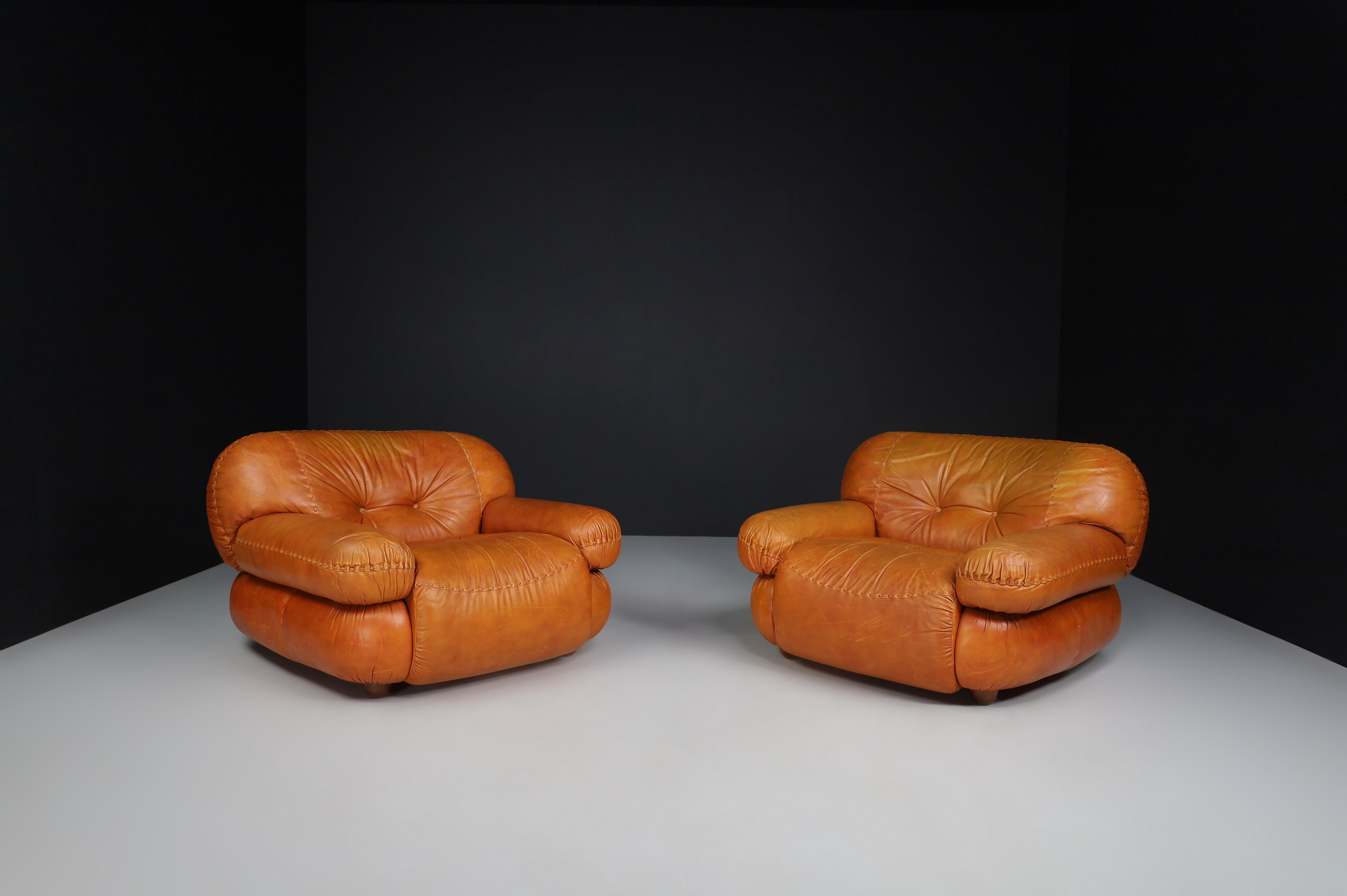 A pair of lounge chairs in cognac brown leather by Sapporo for Mobil Girgi, Italy, in the 1970s. 

Pair of big, fluffy, stylish lounge armchairs that feature round lines and shapes invite you to take a seat and relax—designed by Sapporo for Mobil
