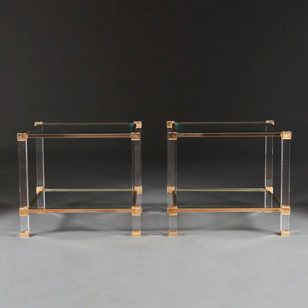 A pair of mid twentieth century lucite two tier tables with brass edges and brass sabots, the glass shelves with beveled edges.