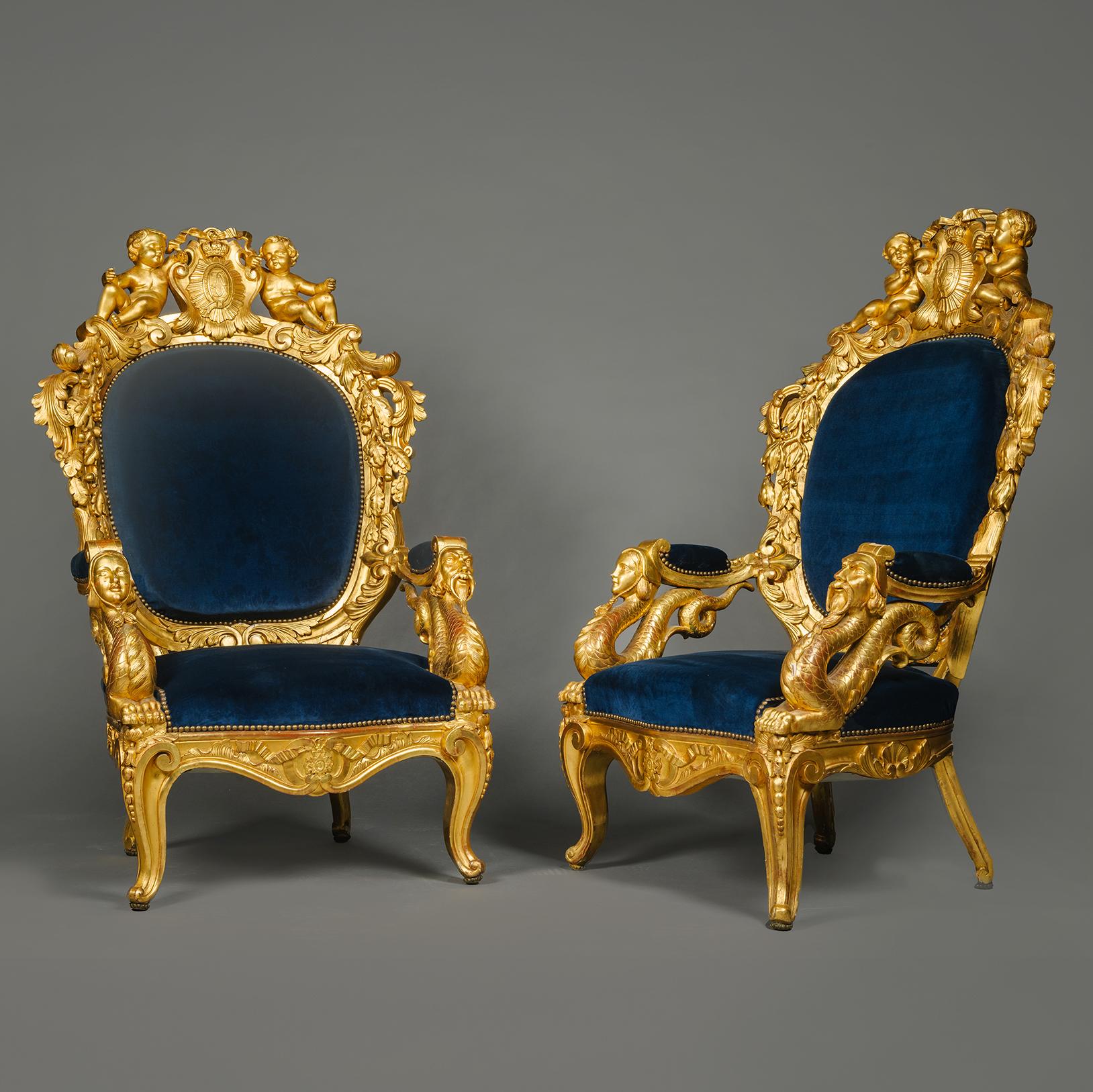 Una coppia di magnifiche poltrone in legno dorato. 

Ogni magnifica sedia da trono ha uno schienale ovale imbottito circondato da un'elaborata crestina intagliata con acanto fiorito, rami di Oak e fleurs-de-lis. La guida superiore presenta due putti