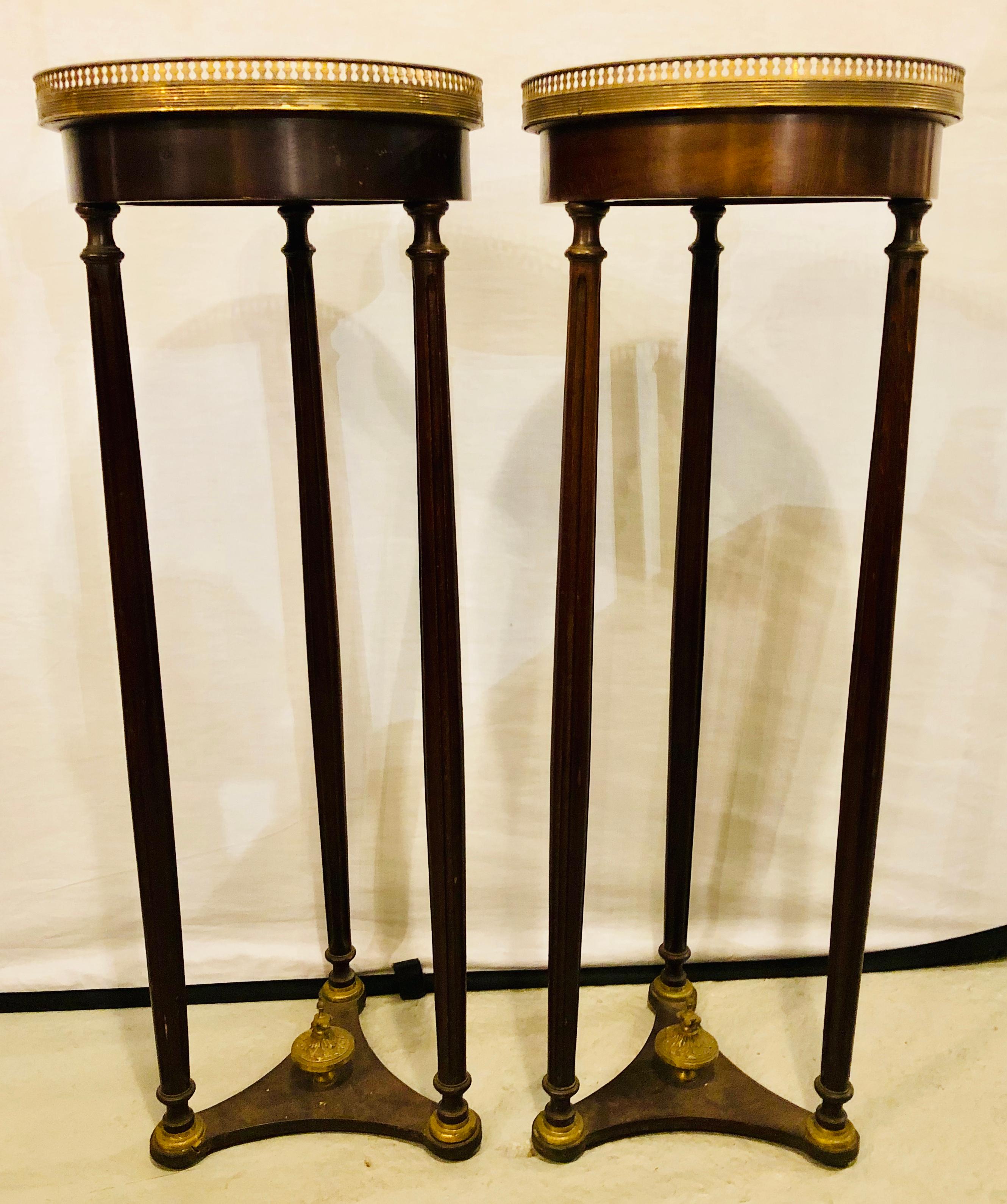 A pair of mahogany Empire marble-top pedestals. Each marble top set in a pierced bronze galley having circular column form legs fastened by a tripod undercarriage with a bronze finial.

Lia\
1gSX/11XA.