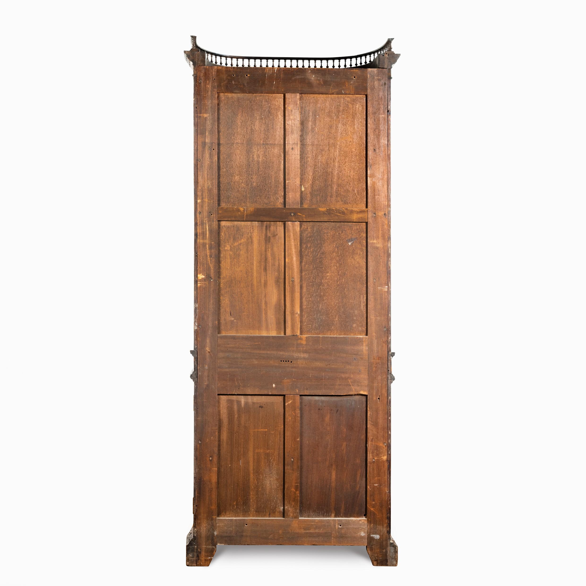A pair of mahogany shaped display cabinets attributed to Gillows, each of tall slender form, the concave front with a glazed upper section enclosing three fitted shelves above cupboard doors carved with an oval field in the manner of Vile and Cobb,