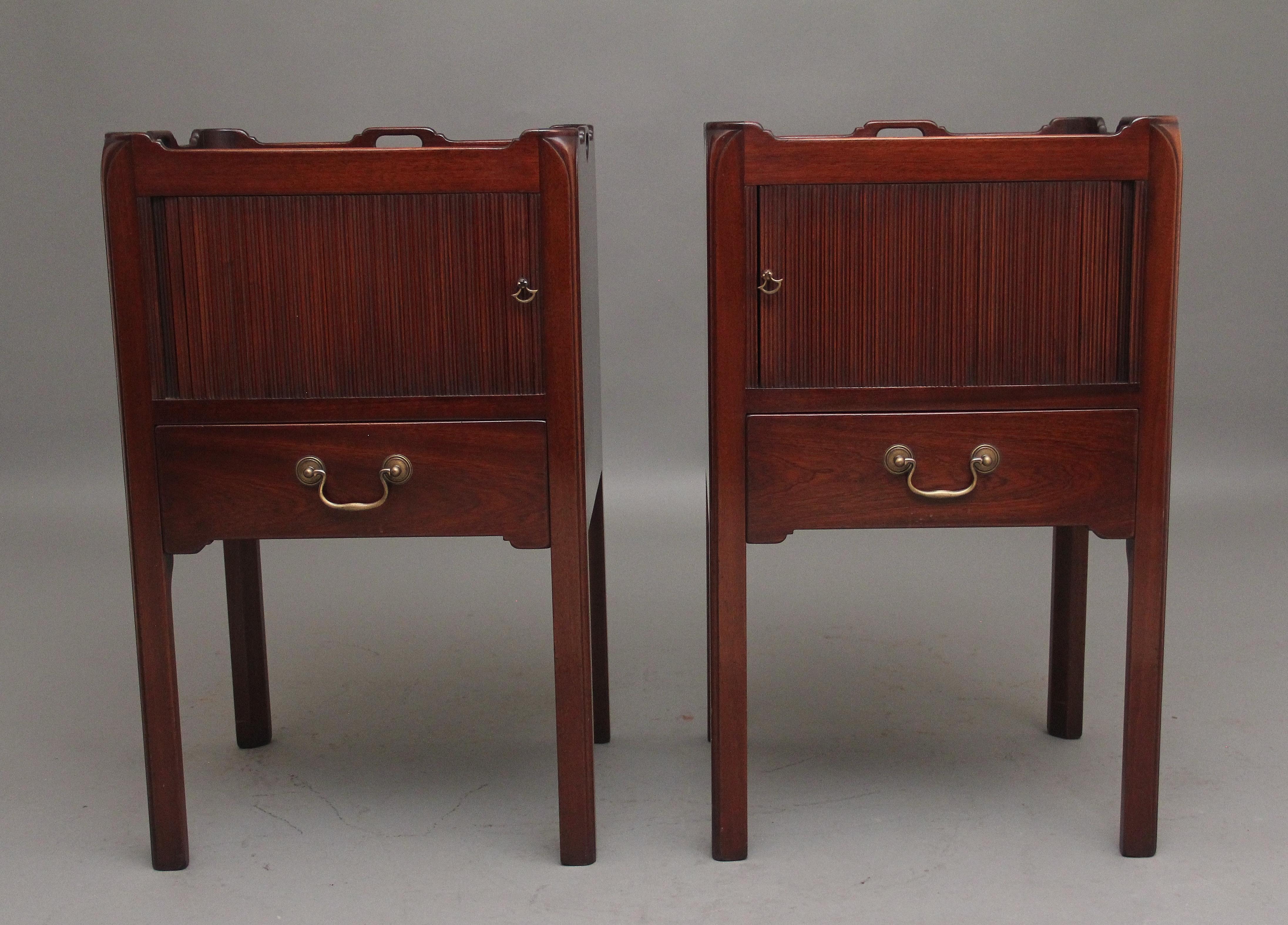 A pair of mahogany tray top bedside cabinets in the Georgian style, having fretted handles on the top moulding, the cupboard below having a tambour front with a mahogany lined drawer below with a brass swan neck handle, standing on chamfered legs. 