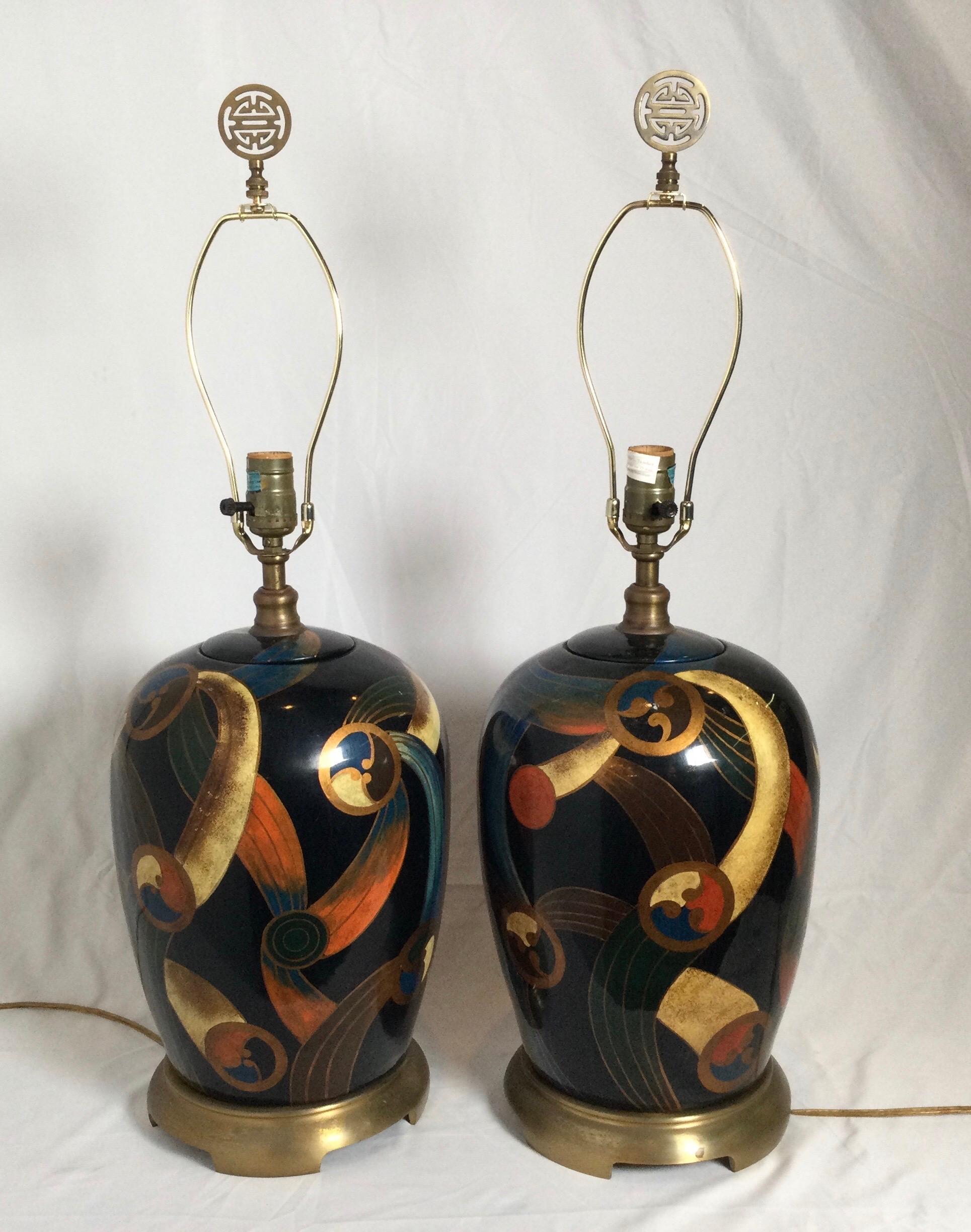 A pair or deco modern style bulbous lamps with a mod hand painted design. The dark background with vibrant color of orange, blue yellow with burnished brass bases. The shades are for photographic purposes only and not included. 26.5 high with a