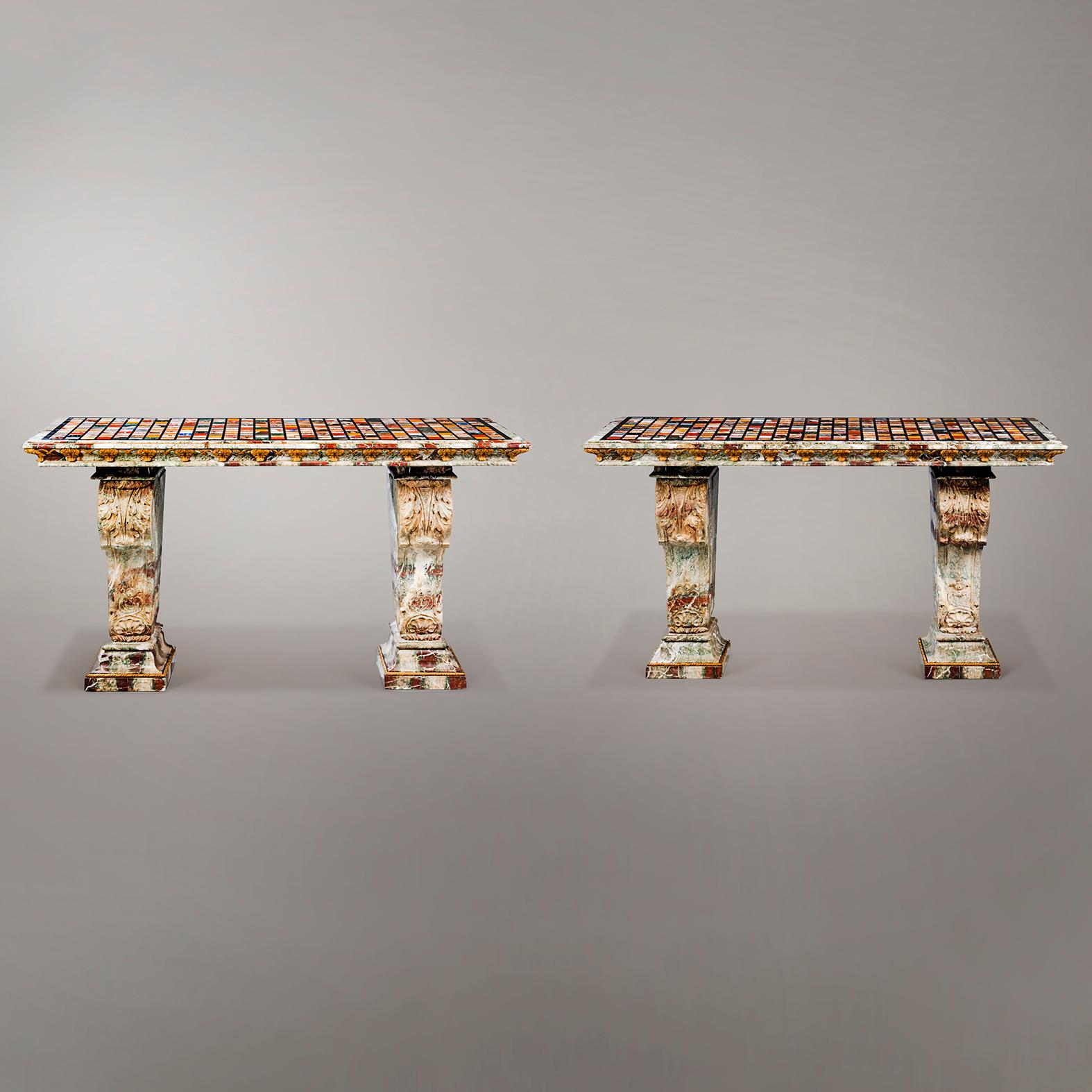 A Pair Of Marble Consoles, With Specimen Marble Tops.

Each with rectangular specimen marble top inset with various marbles and semi-precious stones. The stepped edge applied with gilt-bronze foliate leaves joined by ribbon ties. The leg supports