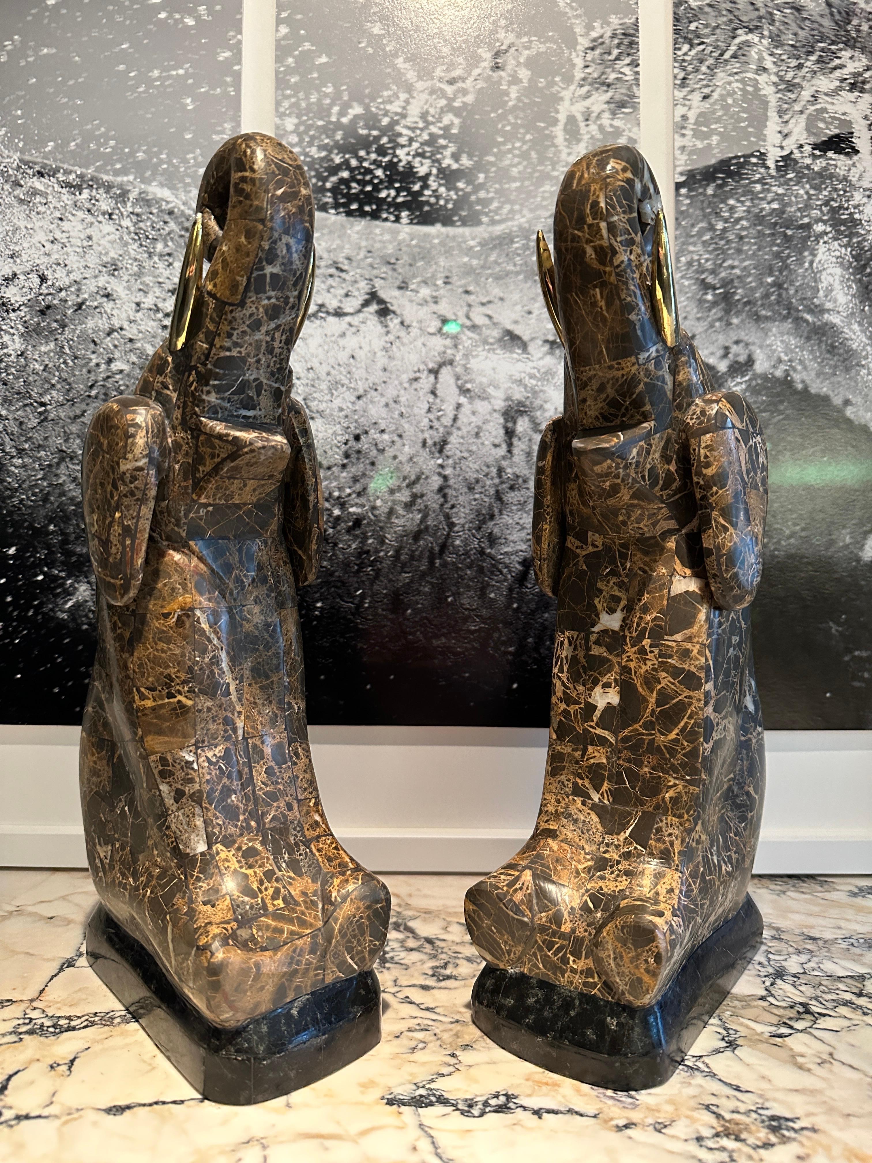 A pair of tessellated Italian Emporador Marble and brass tusked elephants by Maitland Smith. Seated with up turned trunks, on black marble bases.
