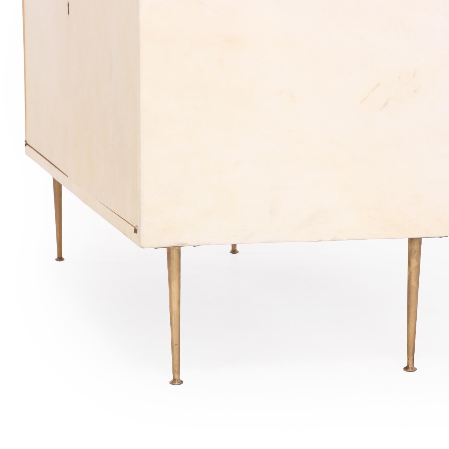 A sophisticated pair of two-door cabinets or nightstands clad in richly toned natural parchment (pergamino). The clean, rectilinear forms are complemented by minimal brass embellishment and short turned legs, allowing the organic texture and warm