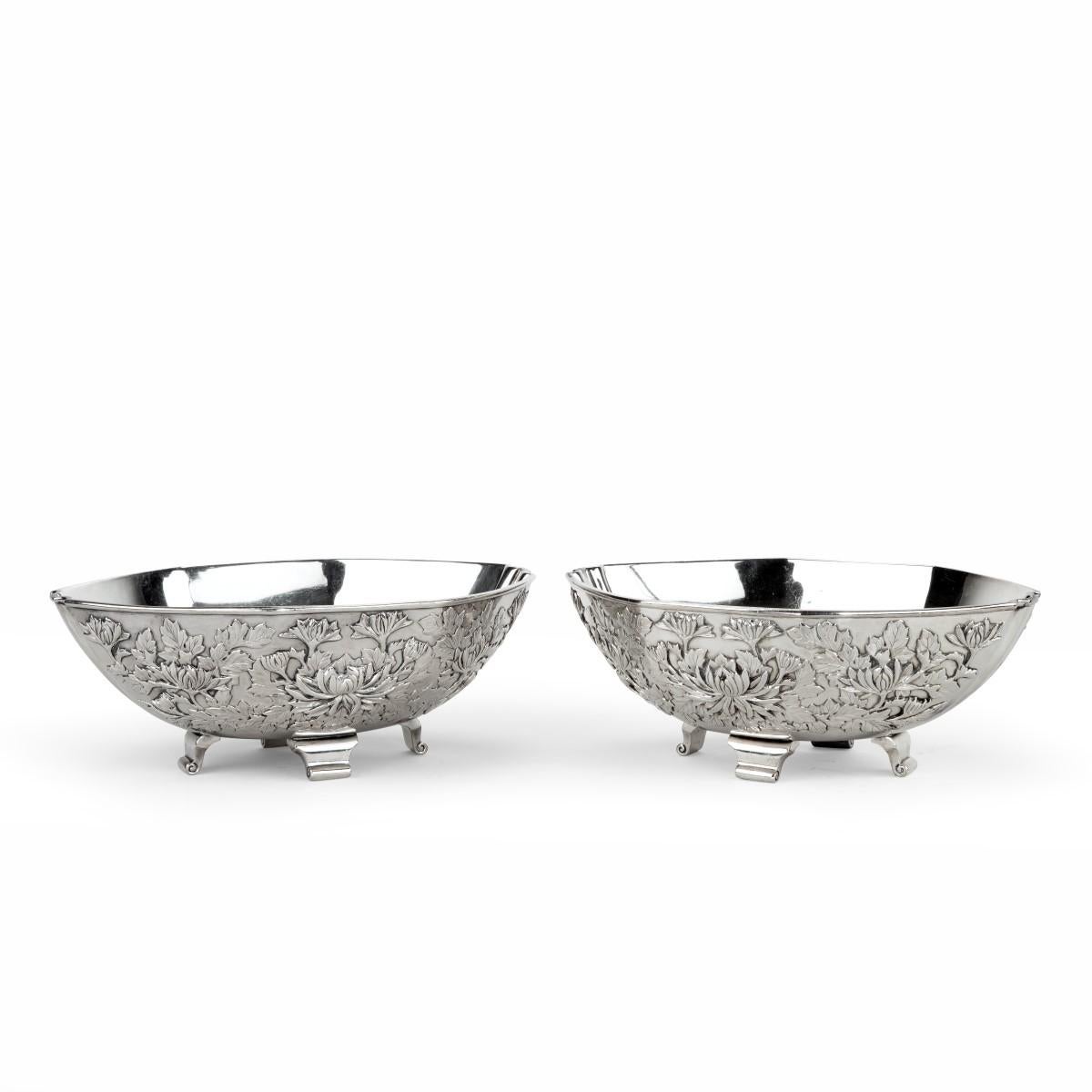A pair of Meiji period solid silver bowls by Eigyoku, each of lobed oval form on four scroll feet, deeply embossed with continuous chrysanthemum heads and leaves. Japanese, circa 1910.