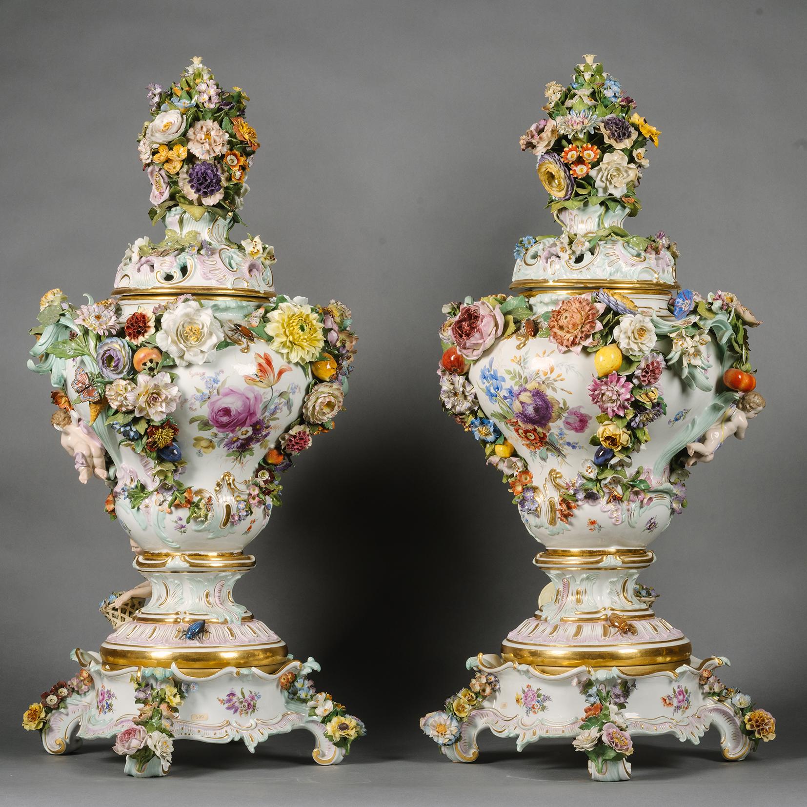 A Pair Of Large Meissen Porcelain Flower-Encrusted Pot-Pourri Vases and Covers On Stands.

Each finial formed as a large bouquet applied with butterflies and insects, above a gilt enriched, pale turquoise and pink pierced rocaille-moulded domed