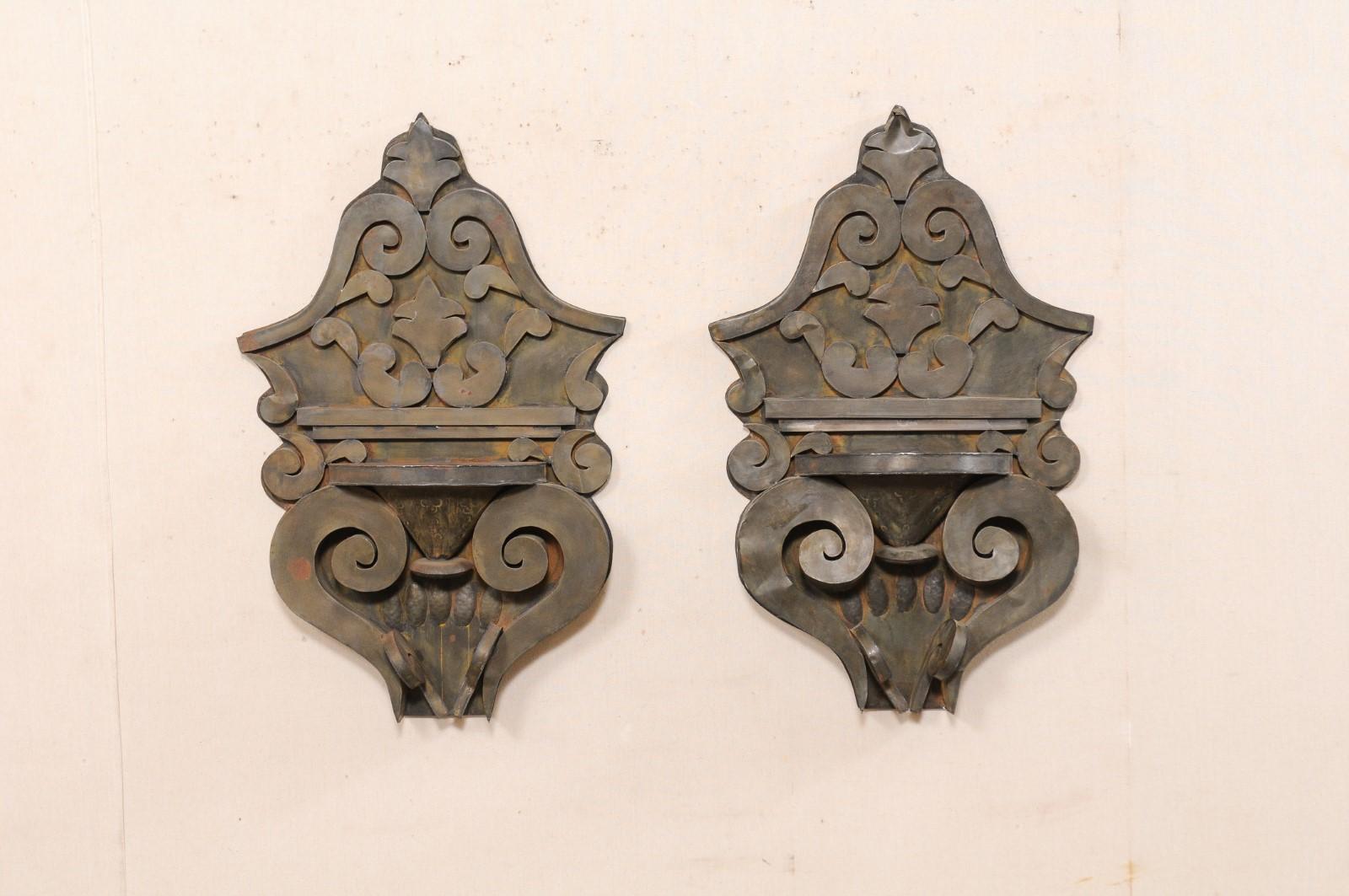 A vintage pair of Mexican tin wall decorations in scrolling design with small shelf. This pair of wall shelves from Mexico have been hand-crafted from old tin, have shapely bodies comprised of volutes, scrolls, and leaf motif. A small half-rounded