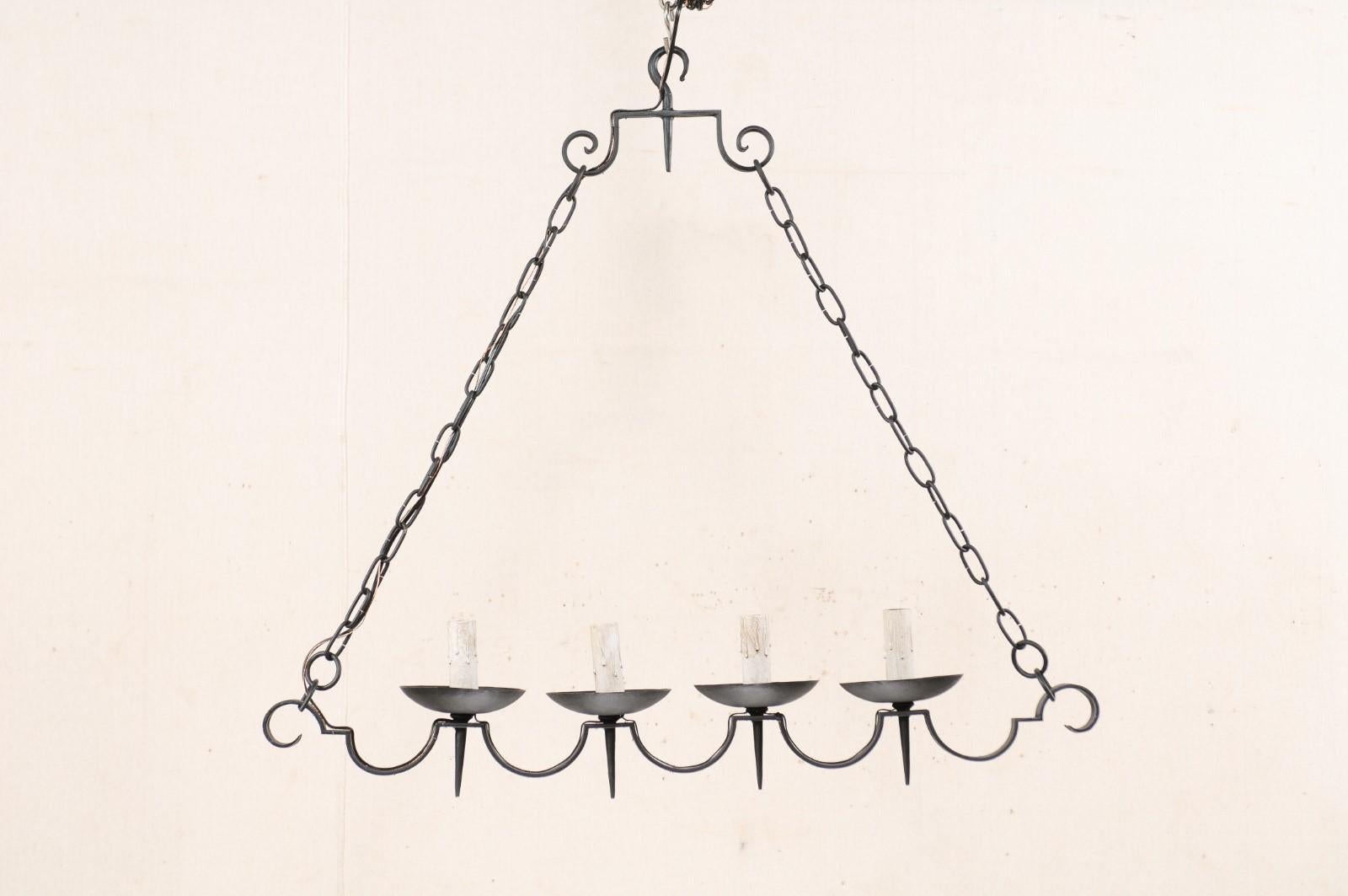 A pair of French black iron four-light chandeliers from the mid-20th century. These vintage chandeliers from France each feature a horizontally positioned scalloped black iron bar, with downward curled ends, with four torch style arms mounted