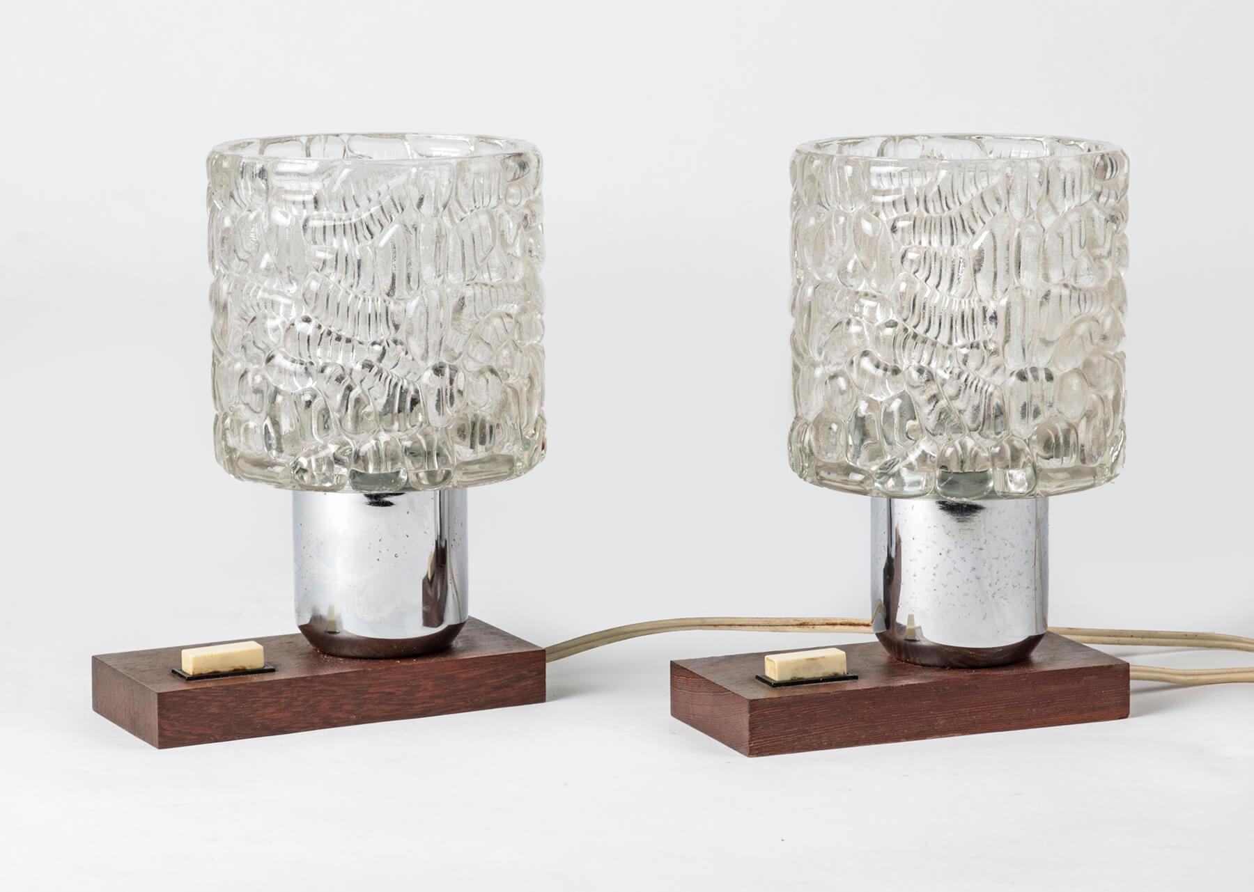 This nice couple of lamps has a modern design from the 1960s or 1970s of the last century. The caps are made of glass and have a relief decoration, which gives a nice effect when the lamps are on. The feet are made of mahogany wood. The lamps are in