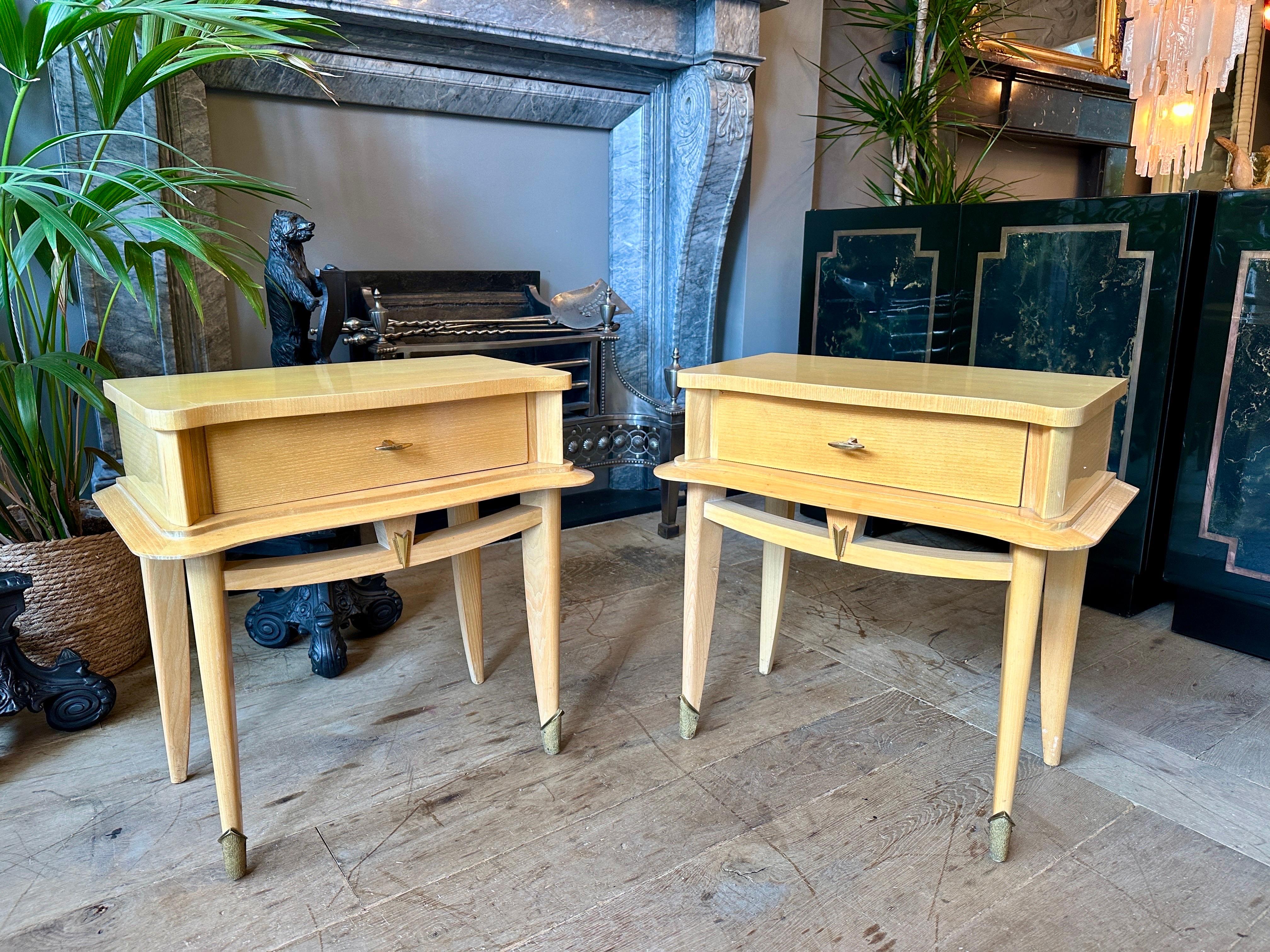 A pair of mid century modern bedside tables or night stands in beech and brass. Very well made with brass sabot feet, brass handles and accents. Sweeping stretcher beneath the draw and in between the legs. A shaped apron surrounding the cabinet.