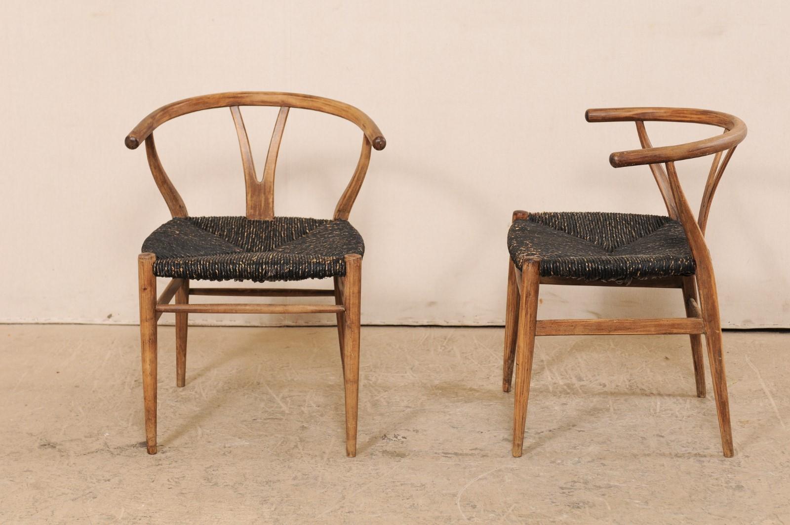 A pair of Danish wood and raffia chairs from the mid-20th century. This vintage pair of Danish occasional chairs have a clean, modern design with smooth wooden wish-bone style backs and curved top rails. Hand-woven raffia, in contrasting dark color,