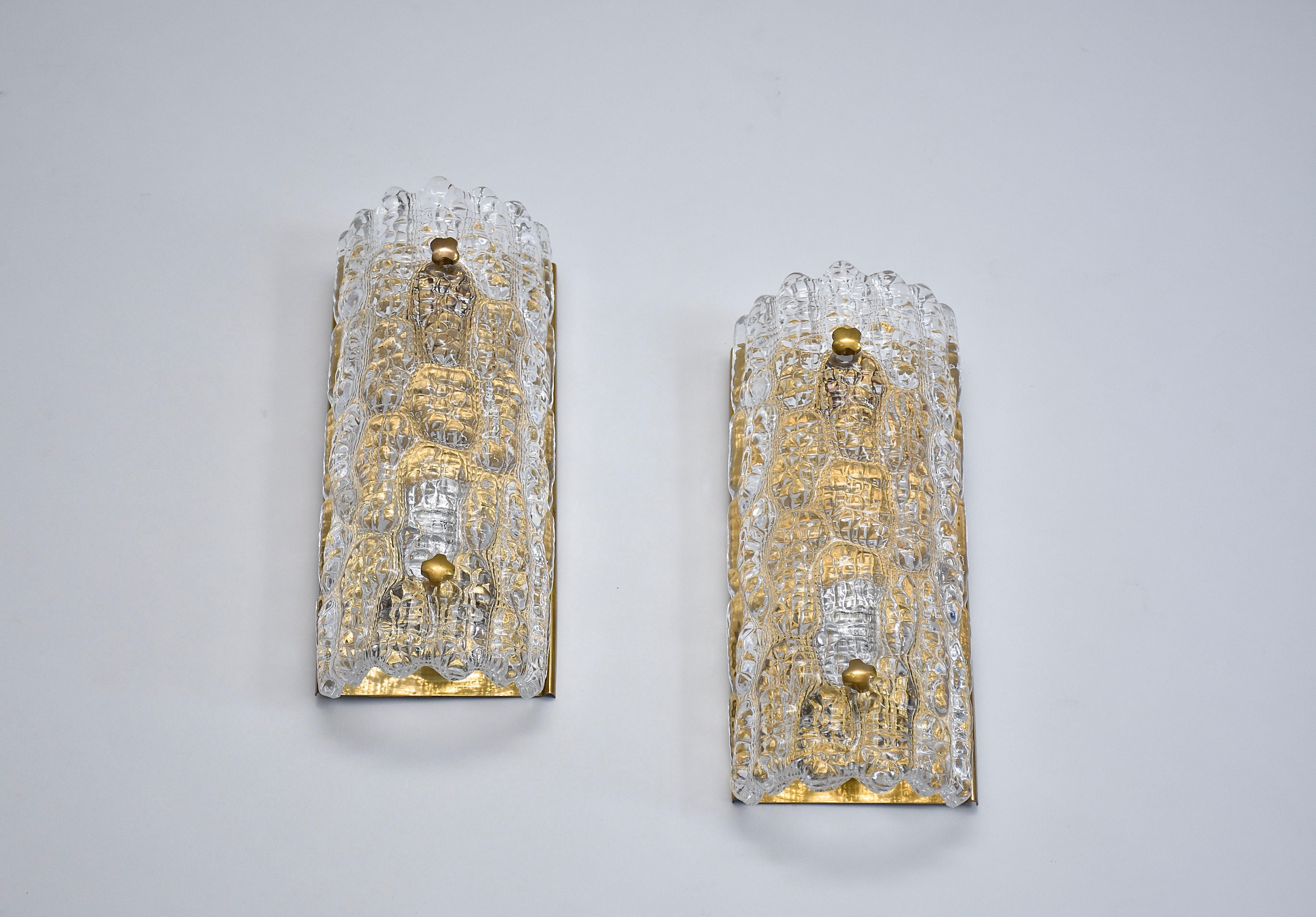 Un bonito par de apliques de latón y cristal diseñados por el diseñador de iluminación sueco Carl Fagerlund y fabricados por Orrefors, famoso fabricante sueco de cristal.
Con hermoso cristal macizo con estructura y placa trasera de latón y botones