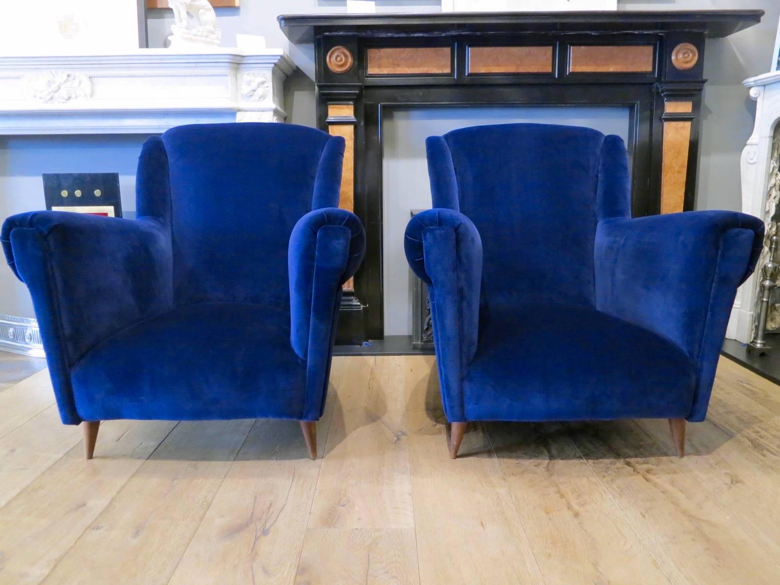 A large and deep pair of midcentury Italian armchairs, with deep seats, winged backs and wooden feet. Recovered in Pierre Frey blue velvet fabric.