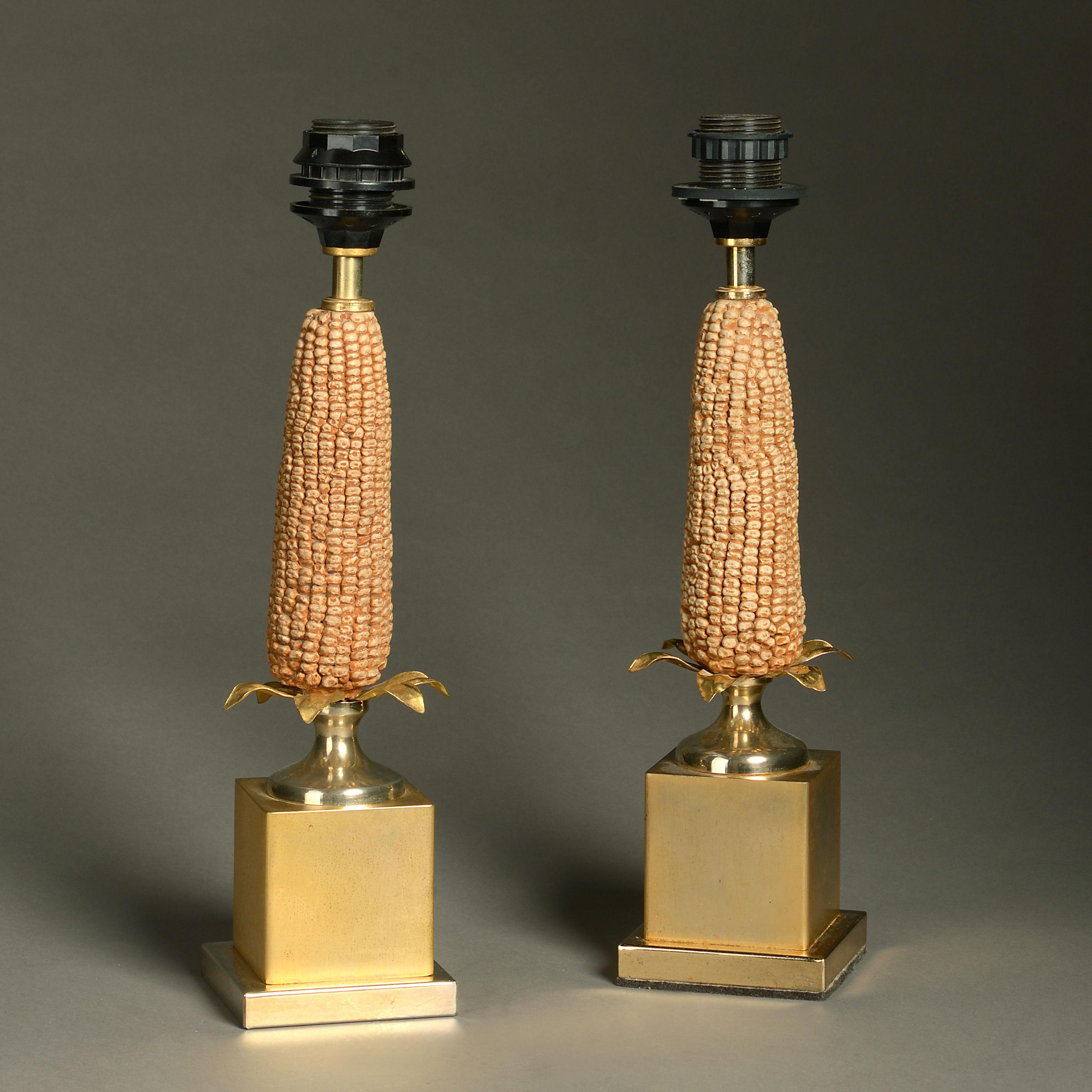 An unusual mid-20th century pair of lamp bases in the manner of Maison Charles, the square gilt metal bases supporting ceramic corn cobs and supporting black shades with gilded interiors. 

Dimensions refer to height of lamp bases (excluding