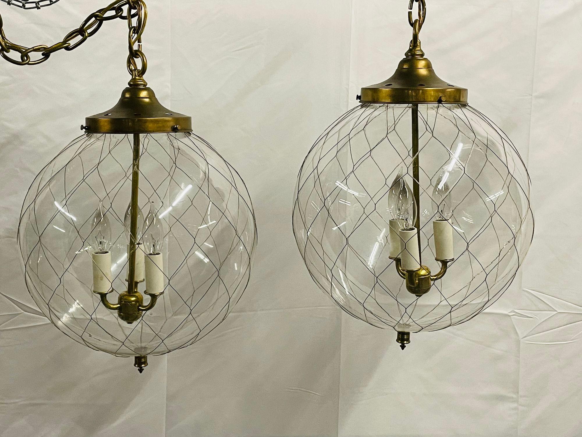 A pair of Mid-Century Modern globe pendants, brass spider web design and hand blown glass.
A finely decorator pair of hand blown glass glove pendant chandeliers. Each having a large hand blown glass circular dome covered in thin bronze reeding