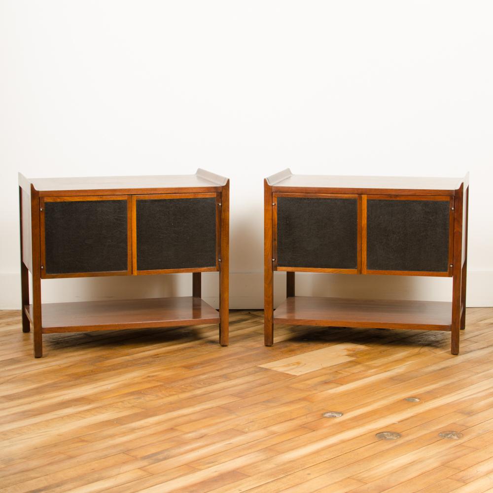 A pair of two-tier Mid-Century Modern walnut side cabinets with leather doors, 1950s.
  