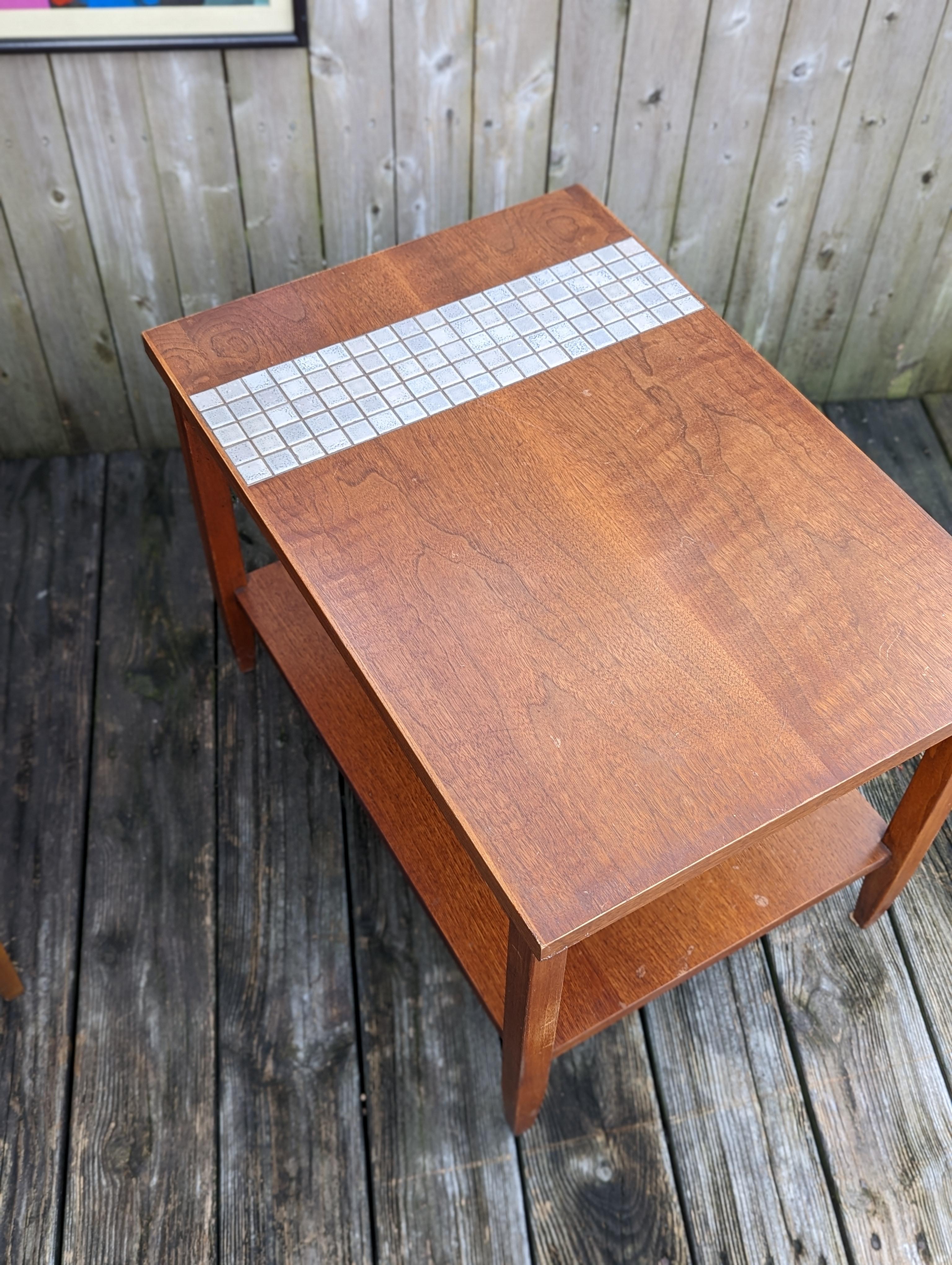 One pair of Mid-Century Modern side tables by Lane Furniture of Alta Vista. Tables feature rich wood grain paired with inlaid tile accents adding to it's era appropriate charm. Each table has a second level shelf which is great for magazines,