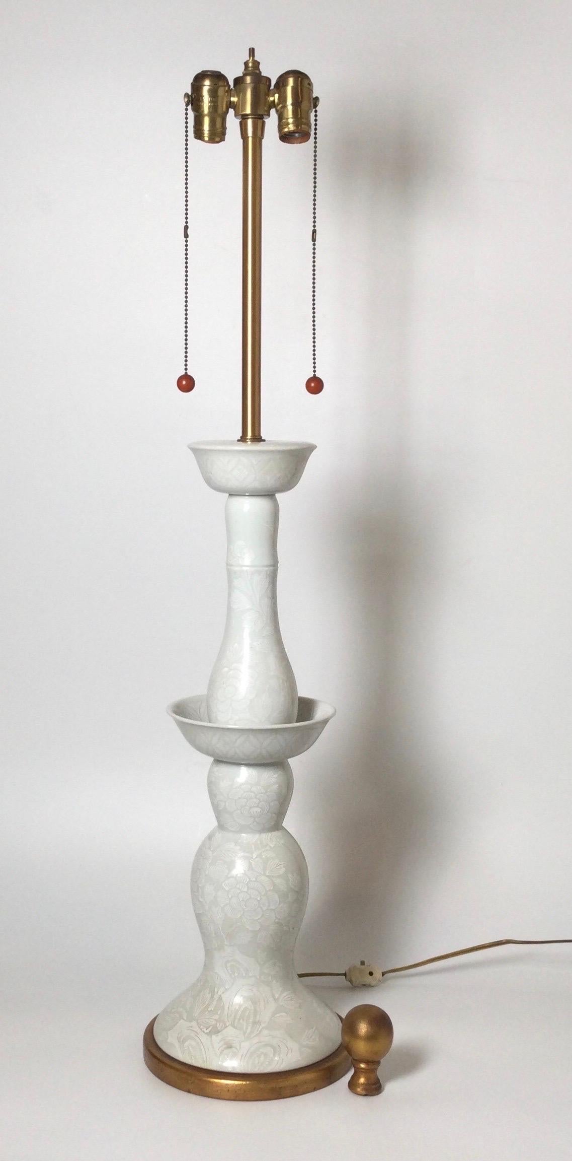 A chic pair of Hollywood regency tall porcelain lamps. The gloss off white porcelain with a pattern on pattern finish in excellent condition. The lamps with sockets for two bulbs. The shades are for photographic purposes only and not included.