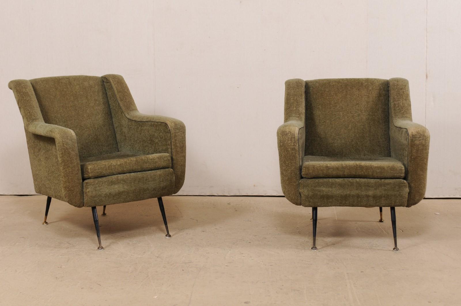 An Italian pair of upholstered club chairs from the mid-20th century. This midcentury pair of armchairs from Italy have a comfortably modern design with squared seats and backs, and a nicely pronounced lip that extends along the sides of the backs