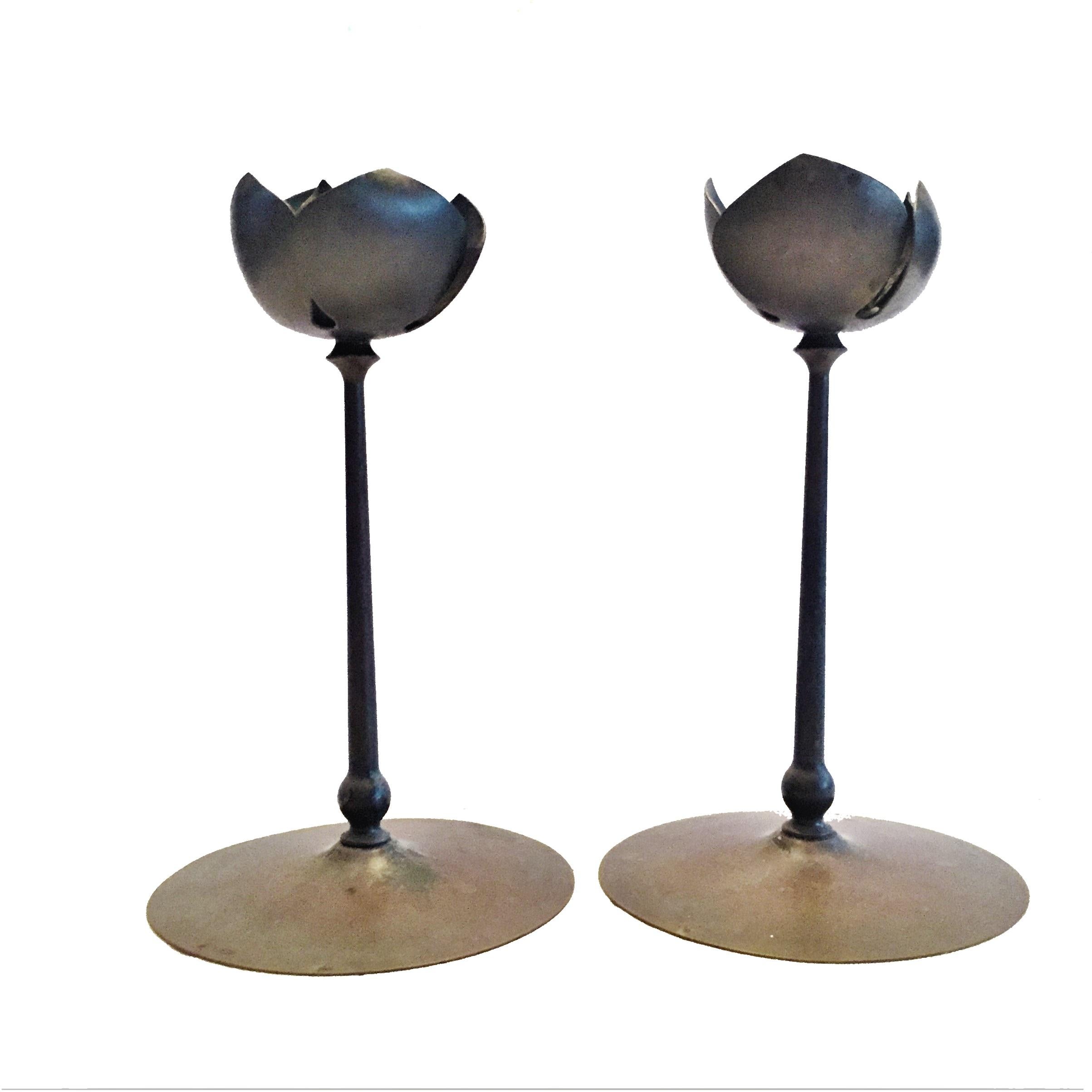 A duo of anodized brass candlesticks, each featuring a round base, stem and a lotus flower that contains a regular size candle. Manufactured in the USA during the 1960s. 

The candlesticks are unpolished, bear the original vintage patina, and