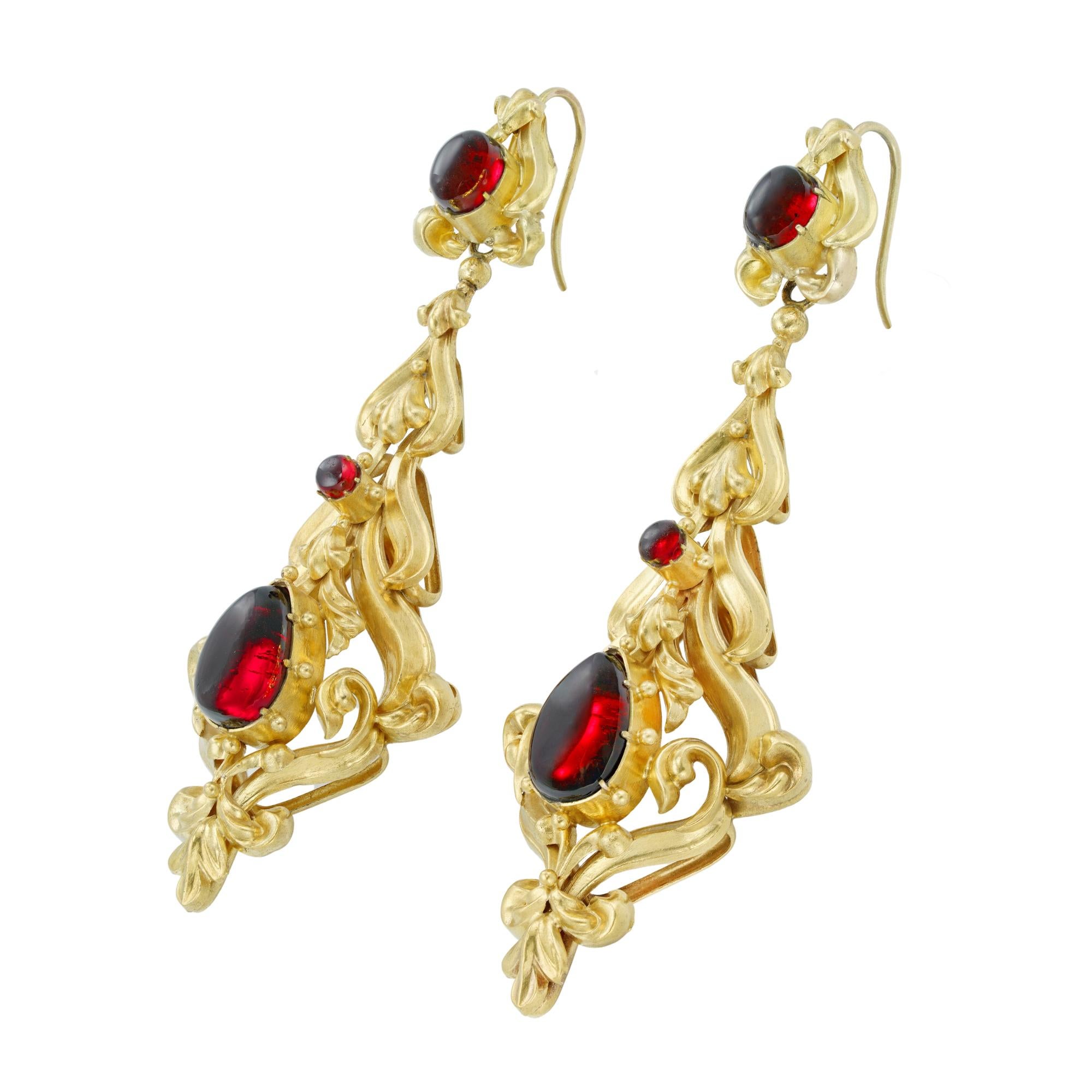 A pair of mid-Victorian garnet and gold earrings, each earring with an ornate scrolled mount, set with and oval, a round and a pear-shaped cabochon garnets, with gold wire fittings, all mounted in 15 carat gold, bearing French Assay marks, circa
